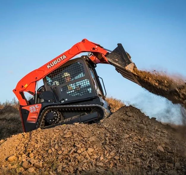 A Kubota mini excavator dumping dirt onto a pile in an outdoor setting.