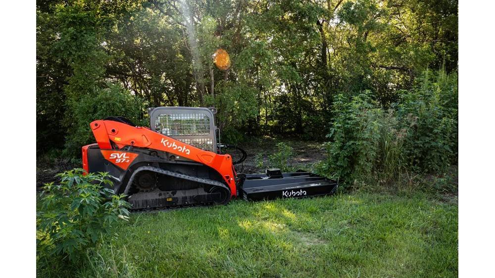 A Kubota SVL 97-2 mini track loader in orange and black parked on grass next to green shrubs and trees.