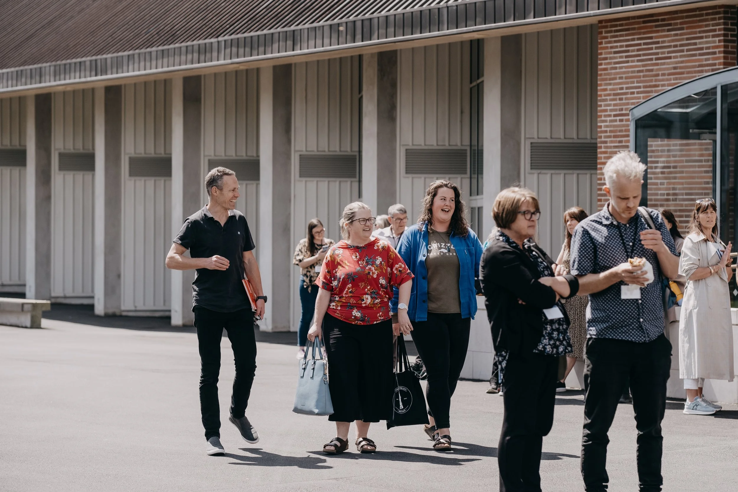 A group of diverse people walking outdoors near a modern building, smiling and talking.