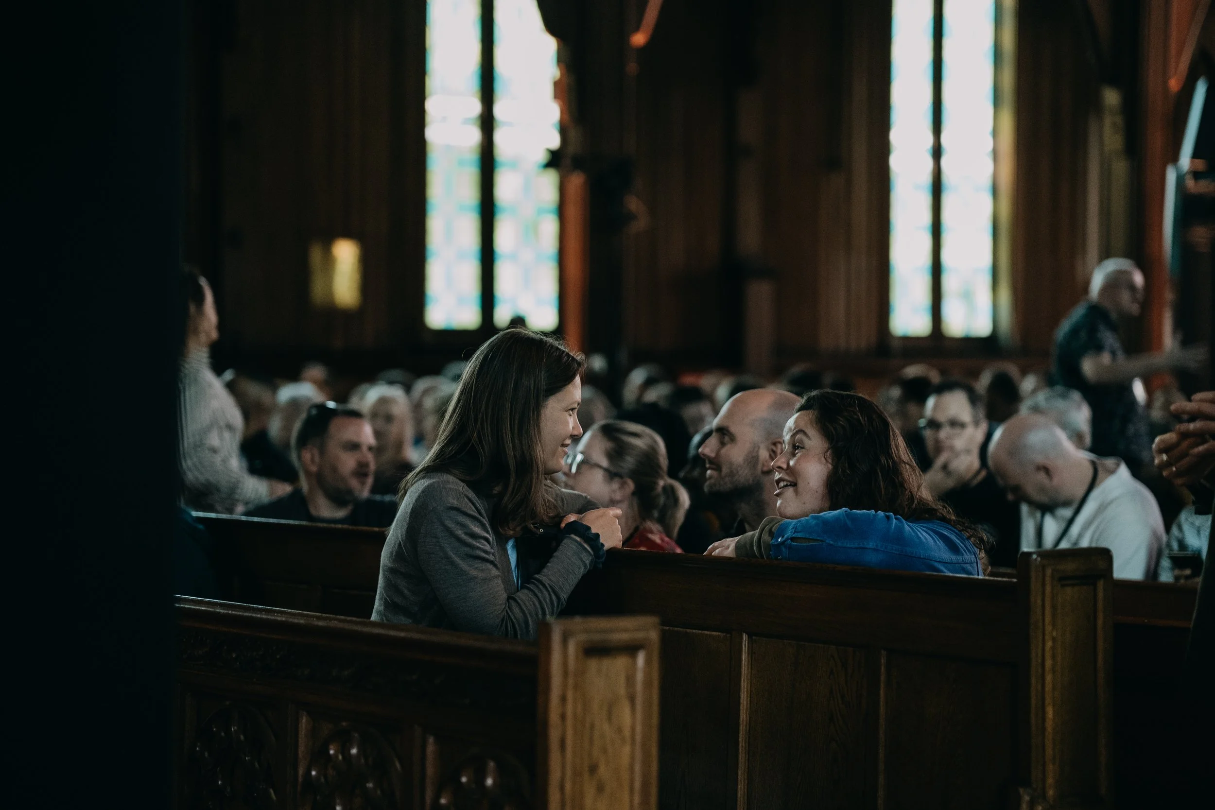 People sitting and talking in a church with stained glass windows in the background.