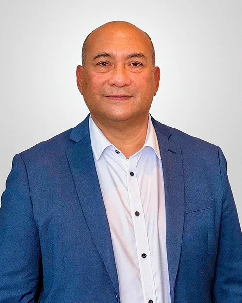 Lui, a middle-aged man with a shaved head wearing a white dress shirt and a blue blazer, standing against a plain light gray background.