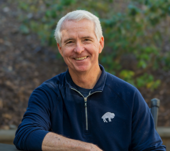 A smiling man with gray hair wearing a navy blue jacket outdoors