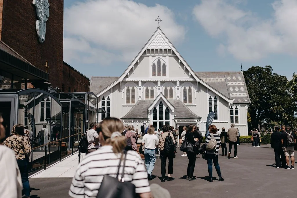 A crowd of people outside a white church with Gothic-style windows and a steeply gabled roof, under a partly cloudy sky.