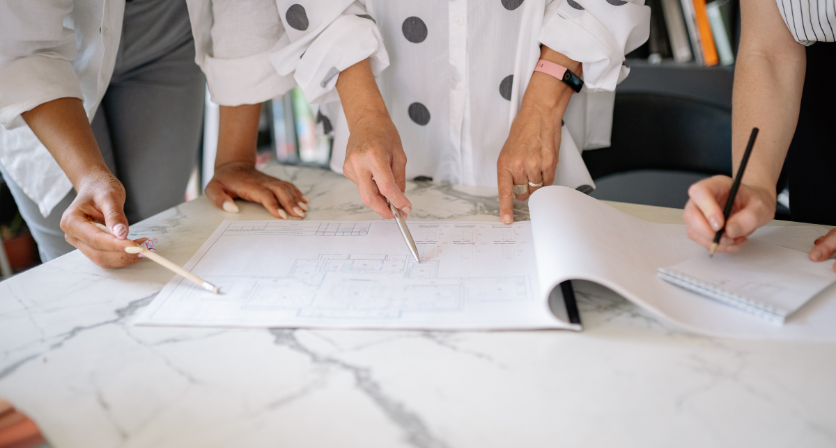 Three people collaborating over architectural blueprints on a marble table.