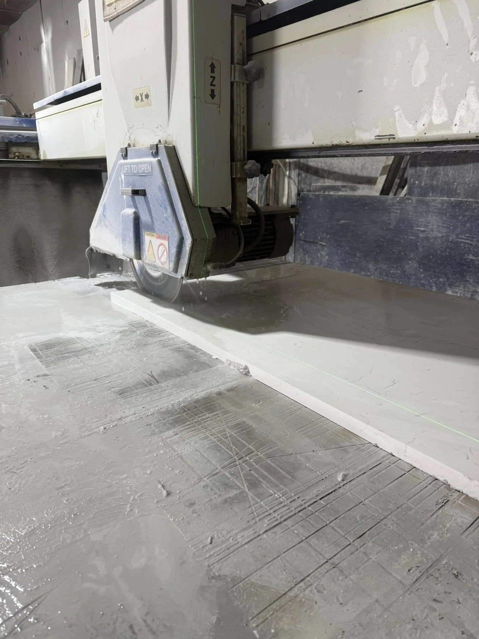 Industrial saw cutting a white material with a green laser guide, with dust and debris on the work surface.