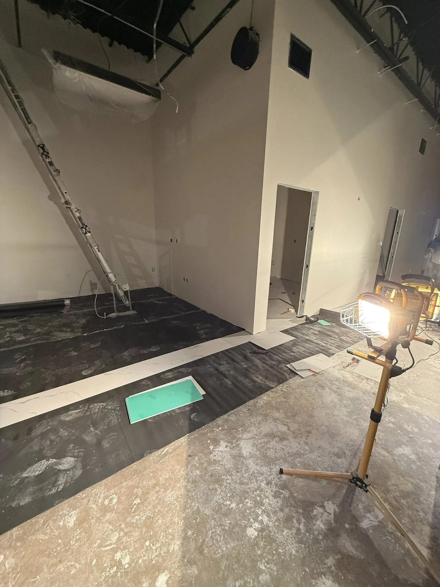 Construction site with drywall and flooring installation in progress, illuminated by a portable work light.