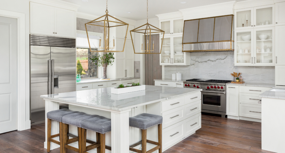 Modern kitchen with white cabinets, stainless steel refrigerator, marble backsplash, kitchen island with seating, gold pendant lights, and wooden floors.