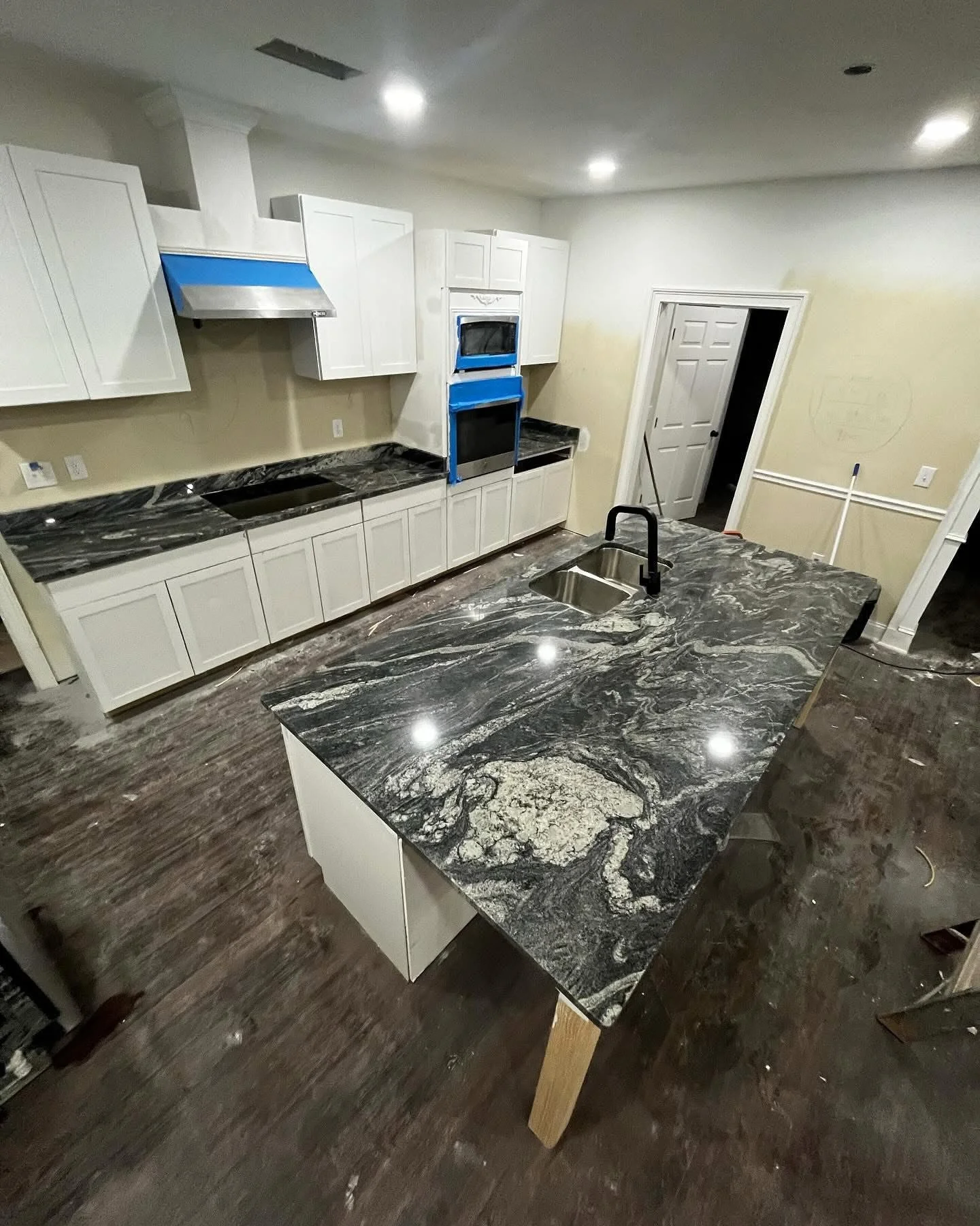 Kitchen with black and white marble countertops, white cabinets, dark wood flooring, and a kitchen island with a black faucet and double sinks.