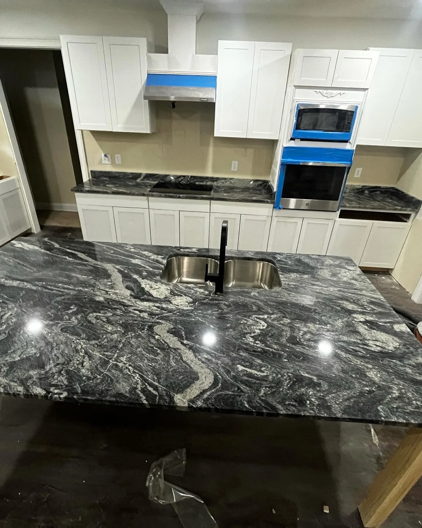 Kitchen with black and white marble countertop, white cabinets, and stainless steel appliances, including a microwave and oven, with blue painter's tape on some cabinets and appliances.
