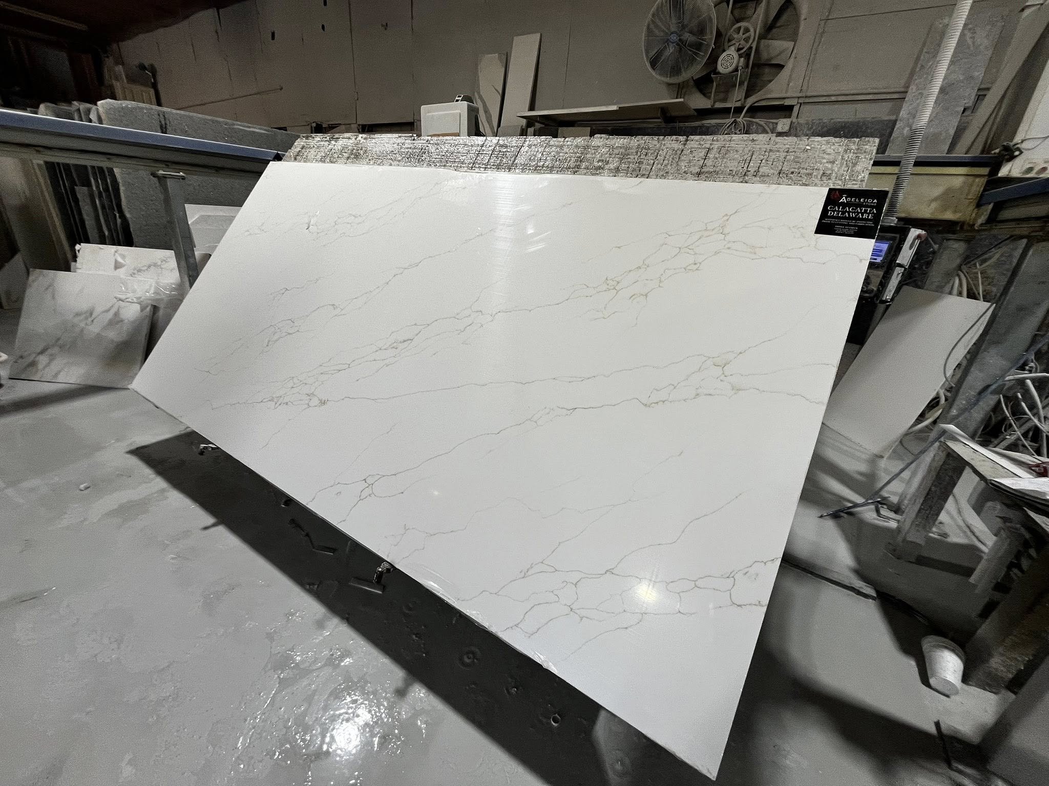 A large white marble slab with gray veining resting on a machine in a workshop.