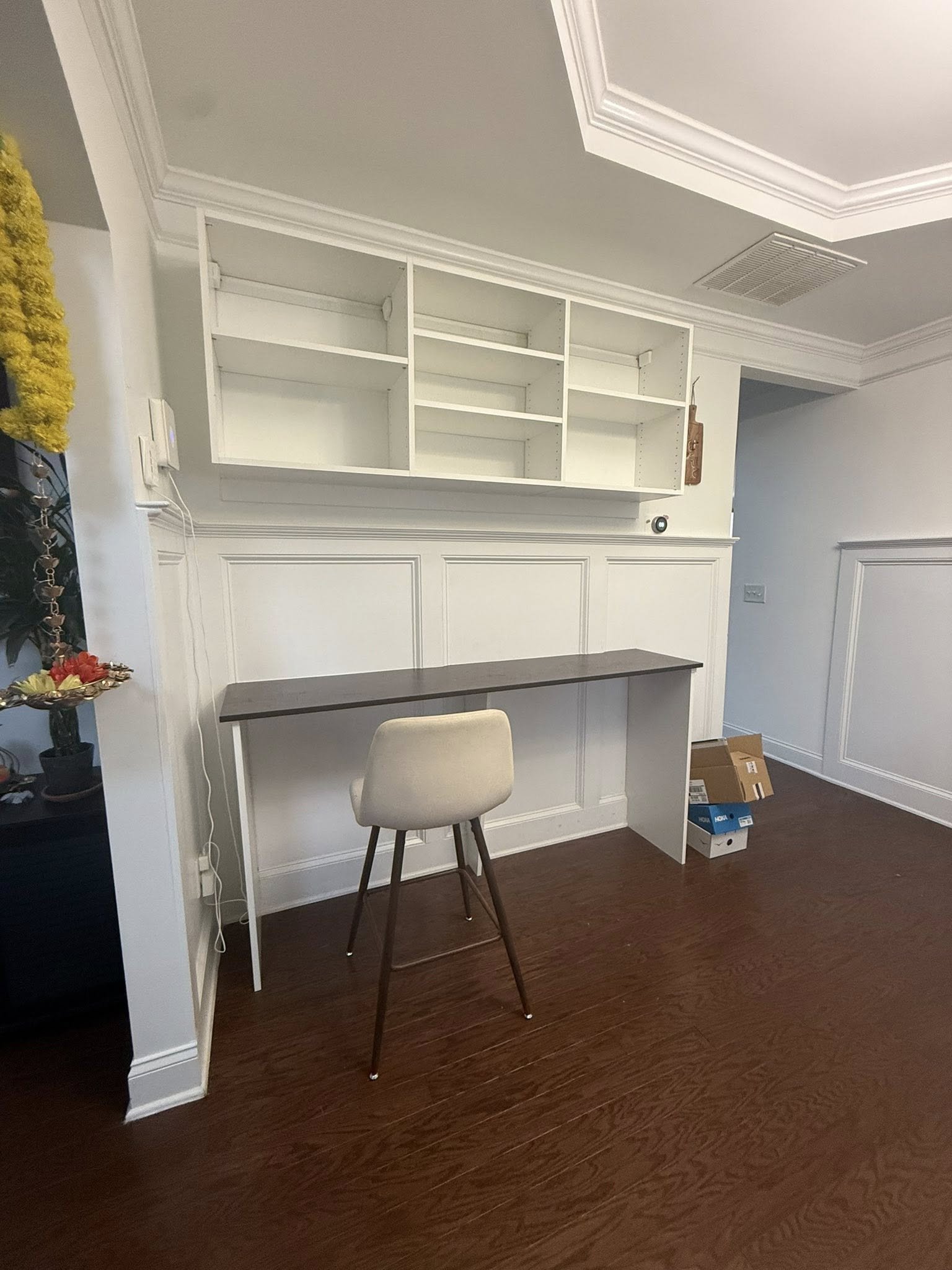 Empty room with a built-in desk and open wall-mounted shelves, a beige chair, and a few boxes on the floor.