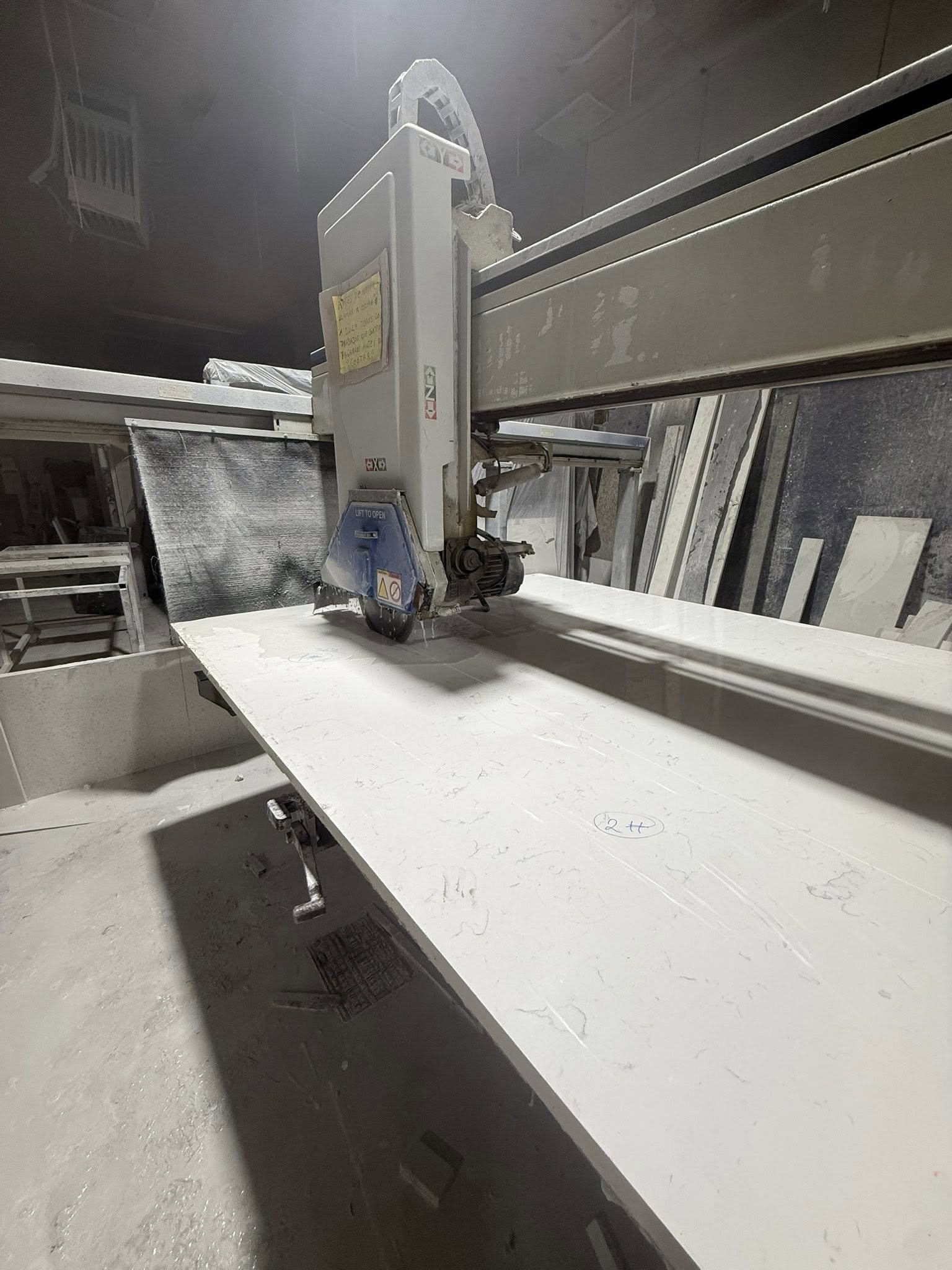 Industrial machine cutting a white marble slab in a workshop.
