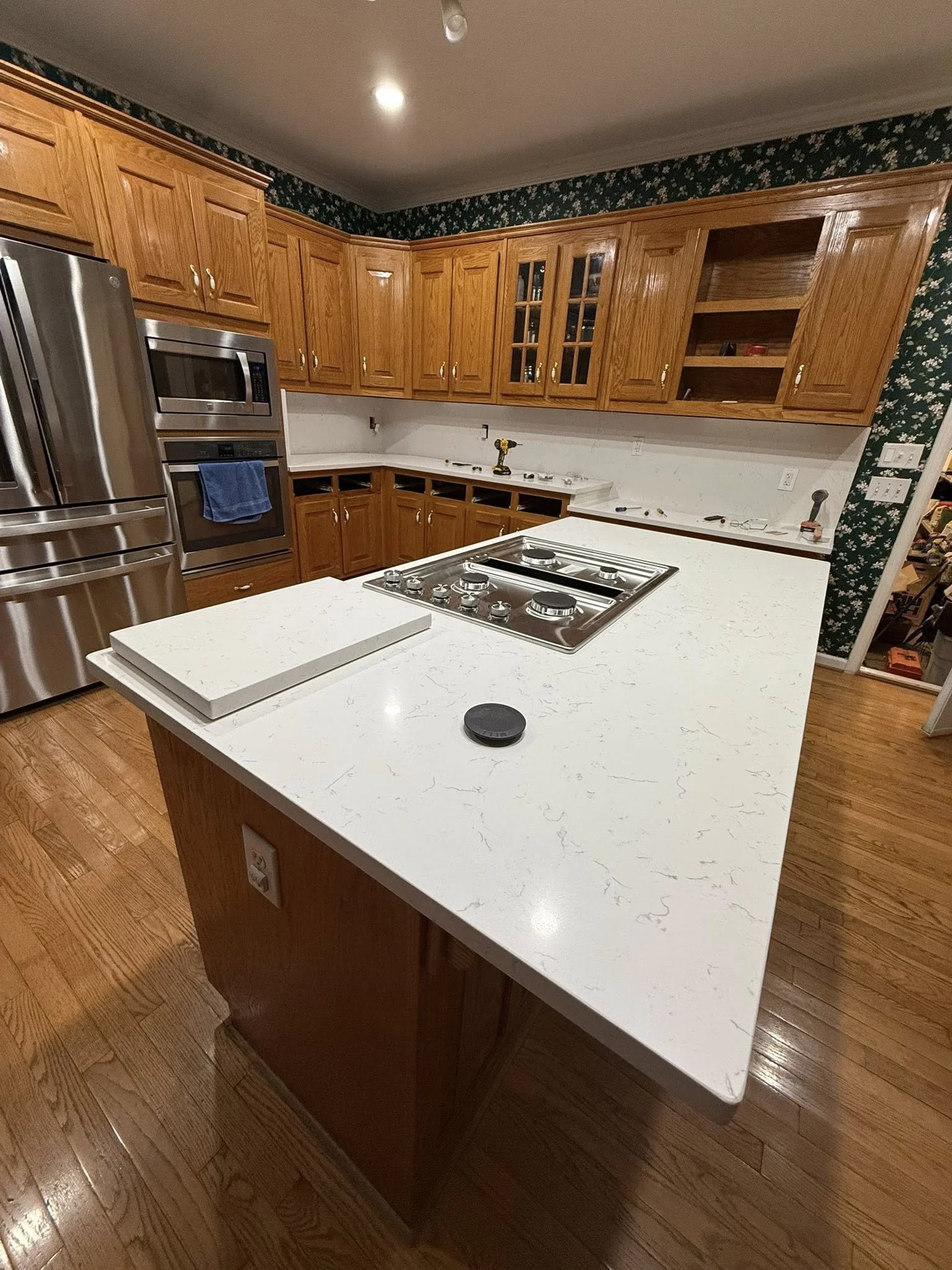 Kitchen with wooden cabinets, a white marble countertop, stainless steel appliances, and a stovetop on the island.
