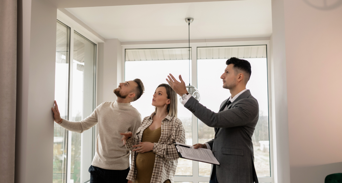 Three people in a modern room with large windows, seemingly discussing or inspecting the space, with one person gesturing as if explaining something.