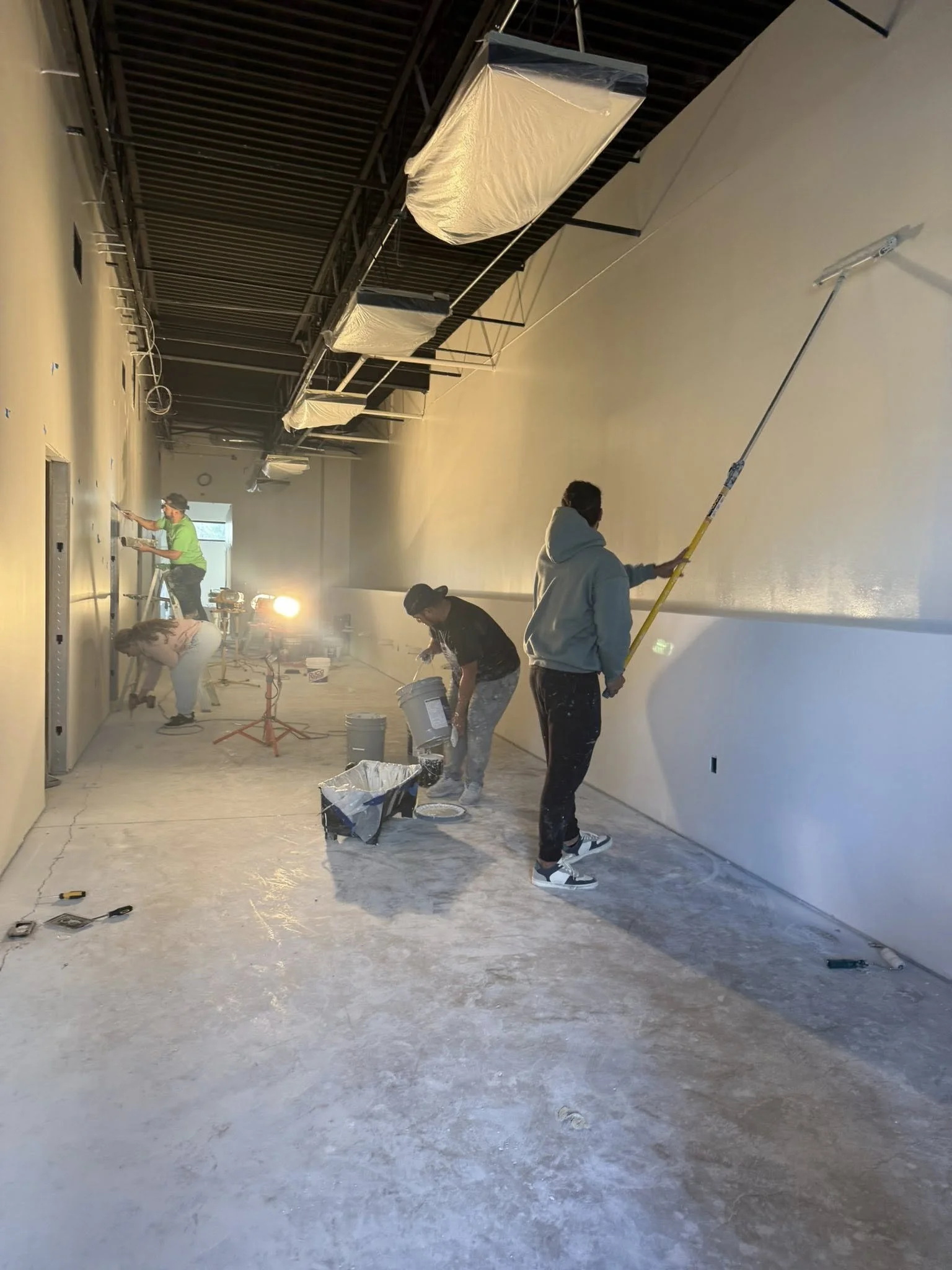 Workers painting walls inside a building under construction or renovation.