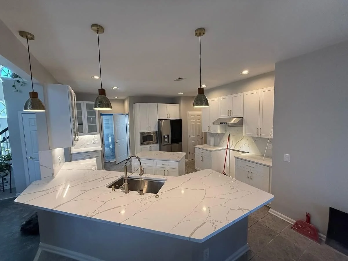 Modern kitchen with white cabinets, marble countertops, stainless steel appliances, pendant lights, and an island with a sink.