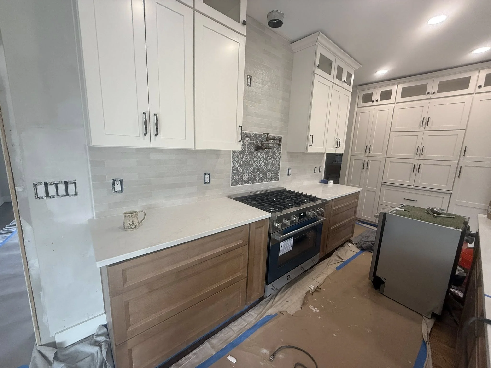 Kitchen under renovation with white and wood cabinets, a stove, and construction materials on the floor.