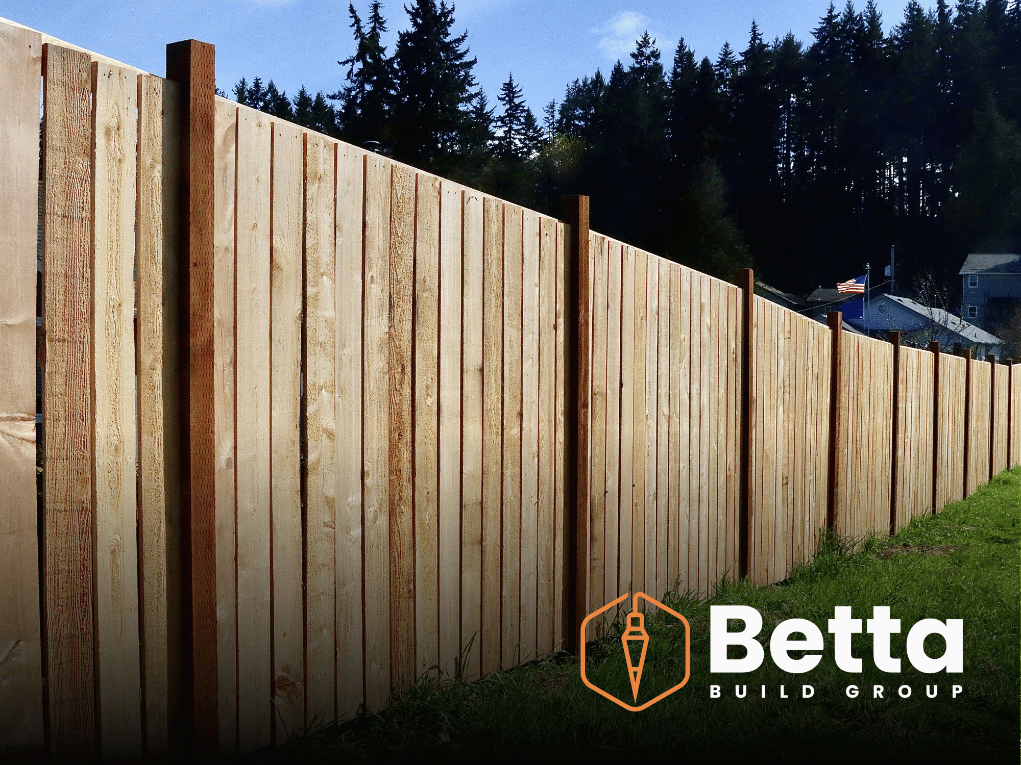 A wooden privacy fence with vertical planks and support posts, set outdoors with trees and houses in the background, under a partly cloudy sky.