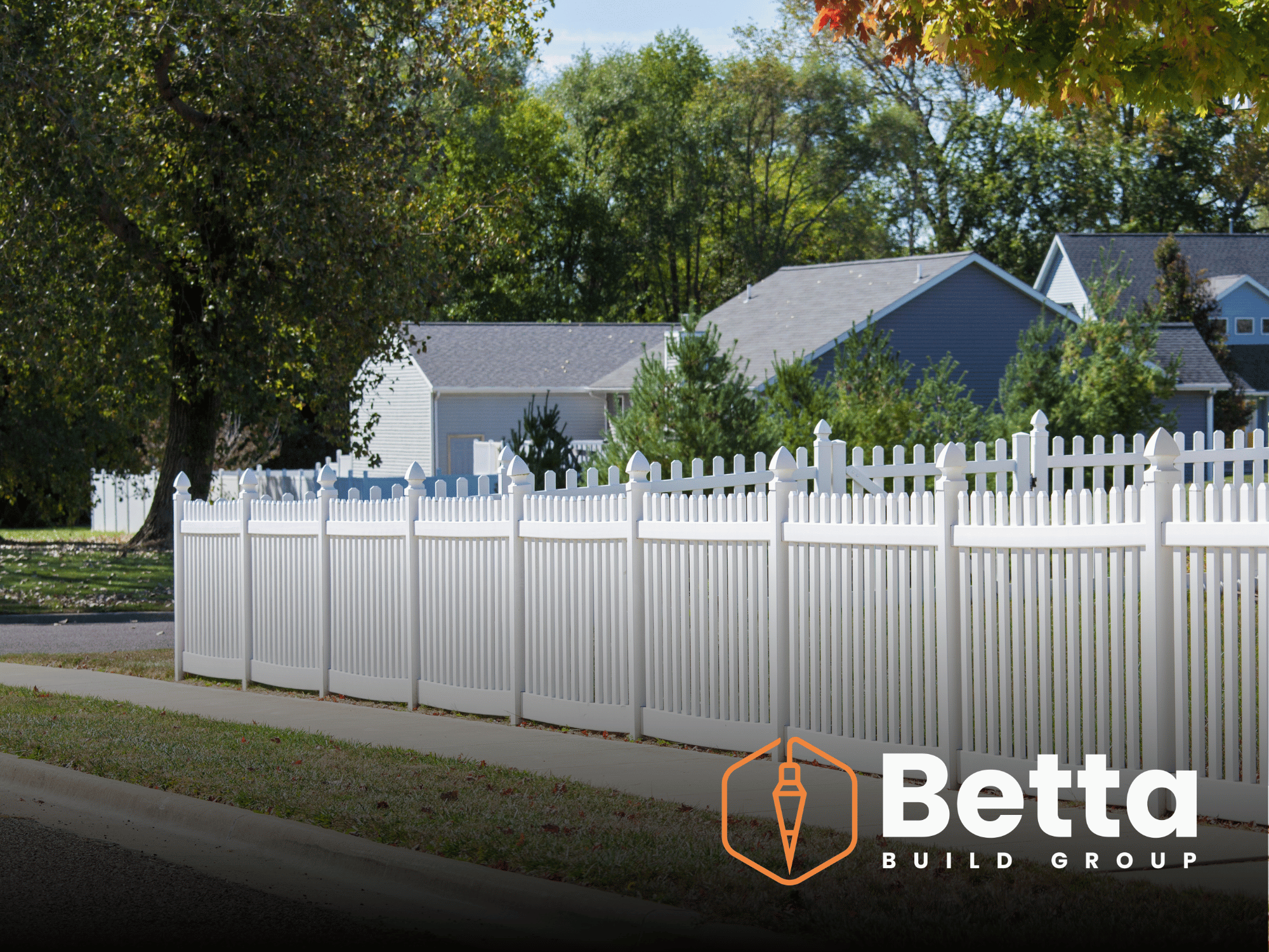 Residential neighborhood with a large white picket fence, trees with autumn leaves, and houses with grey and blue roofs.