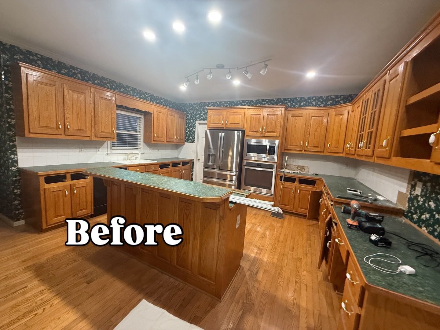 Empty kitchen with wooden cabinets, green countertops, and hardwood flooring, before renovation.