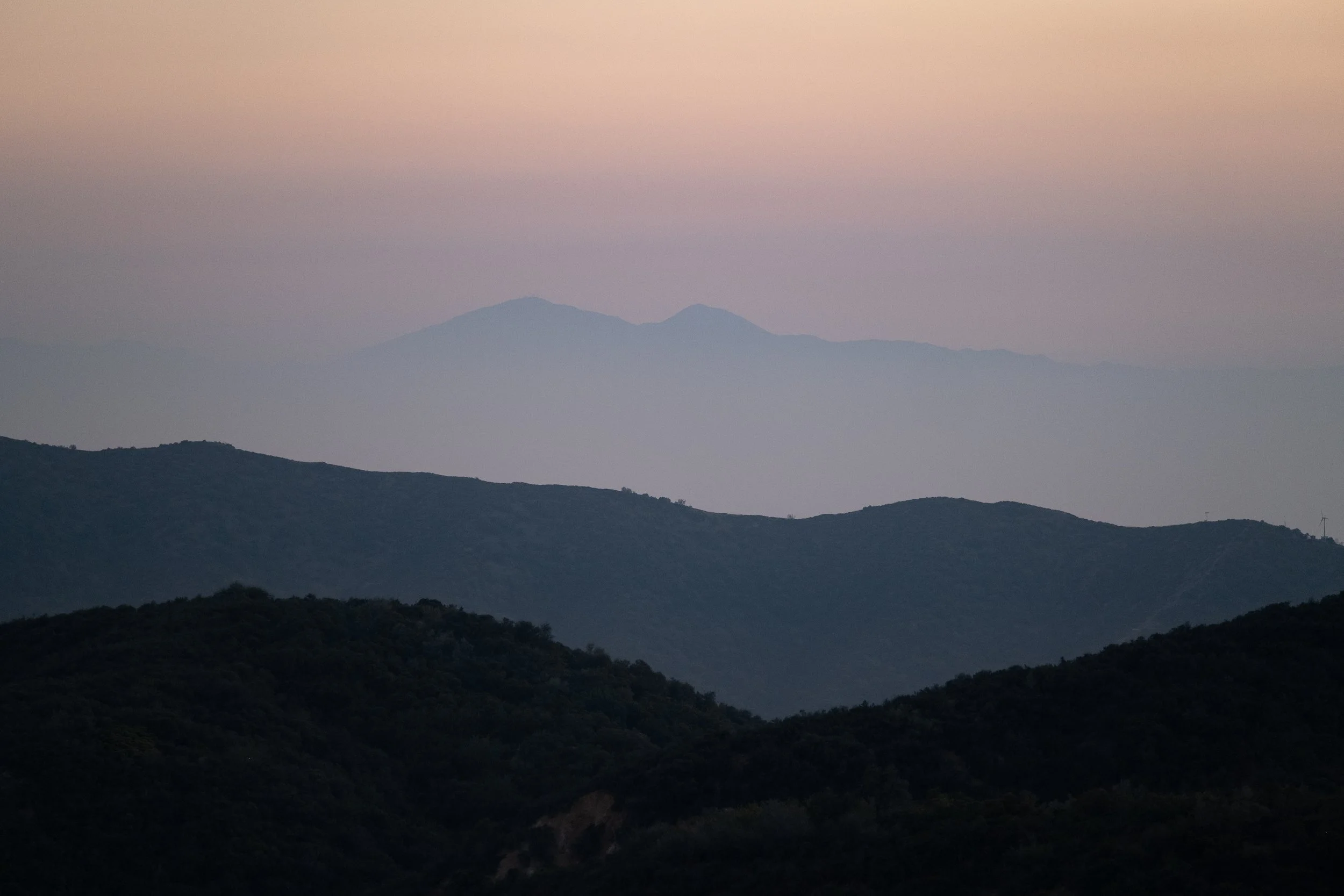 A landscape of rolling hills and distant mountains under a pinkish sky at dusk or dawn.