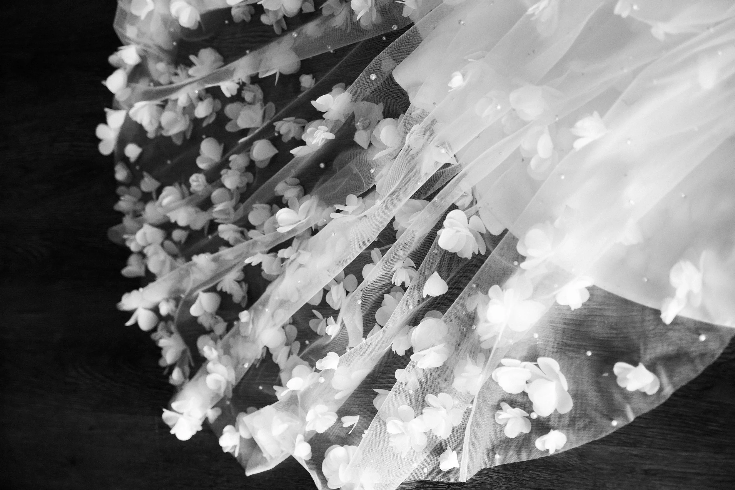 Black and white photo of delicate fabric with small floral embellishments on a dark wooden surface.