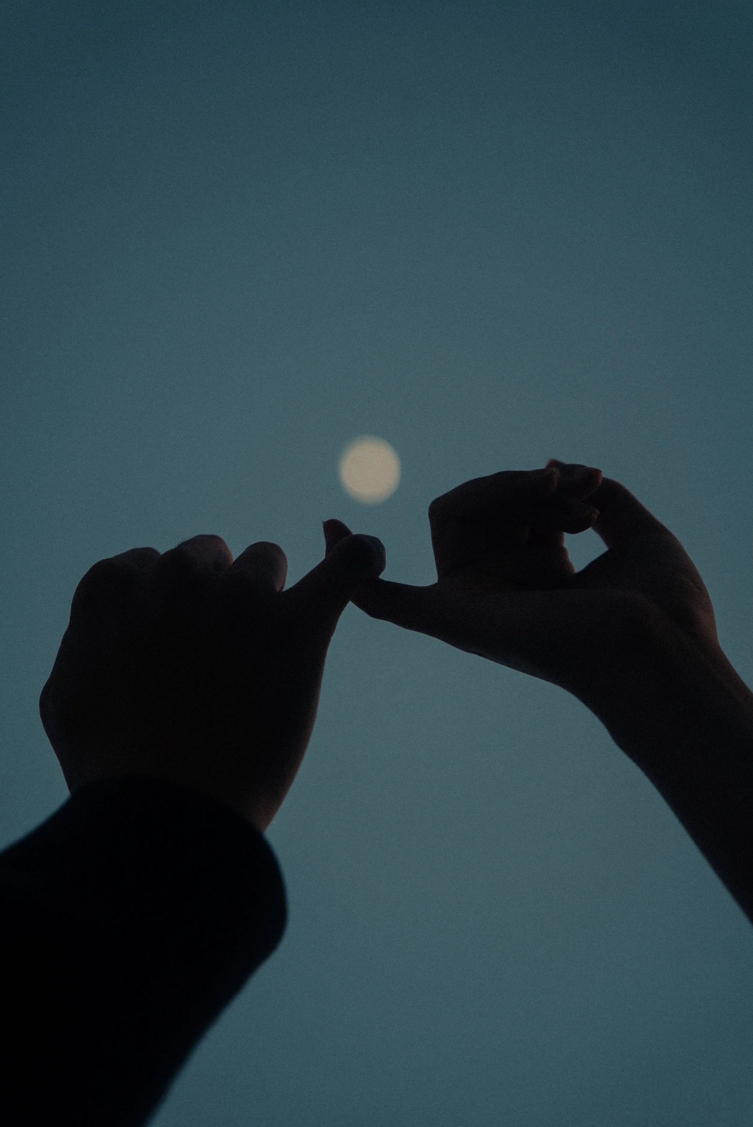 Silhouette of hands fingers touching against a moonlit sky.