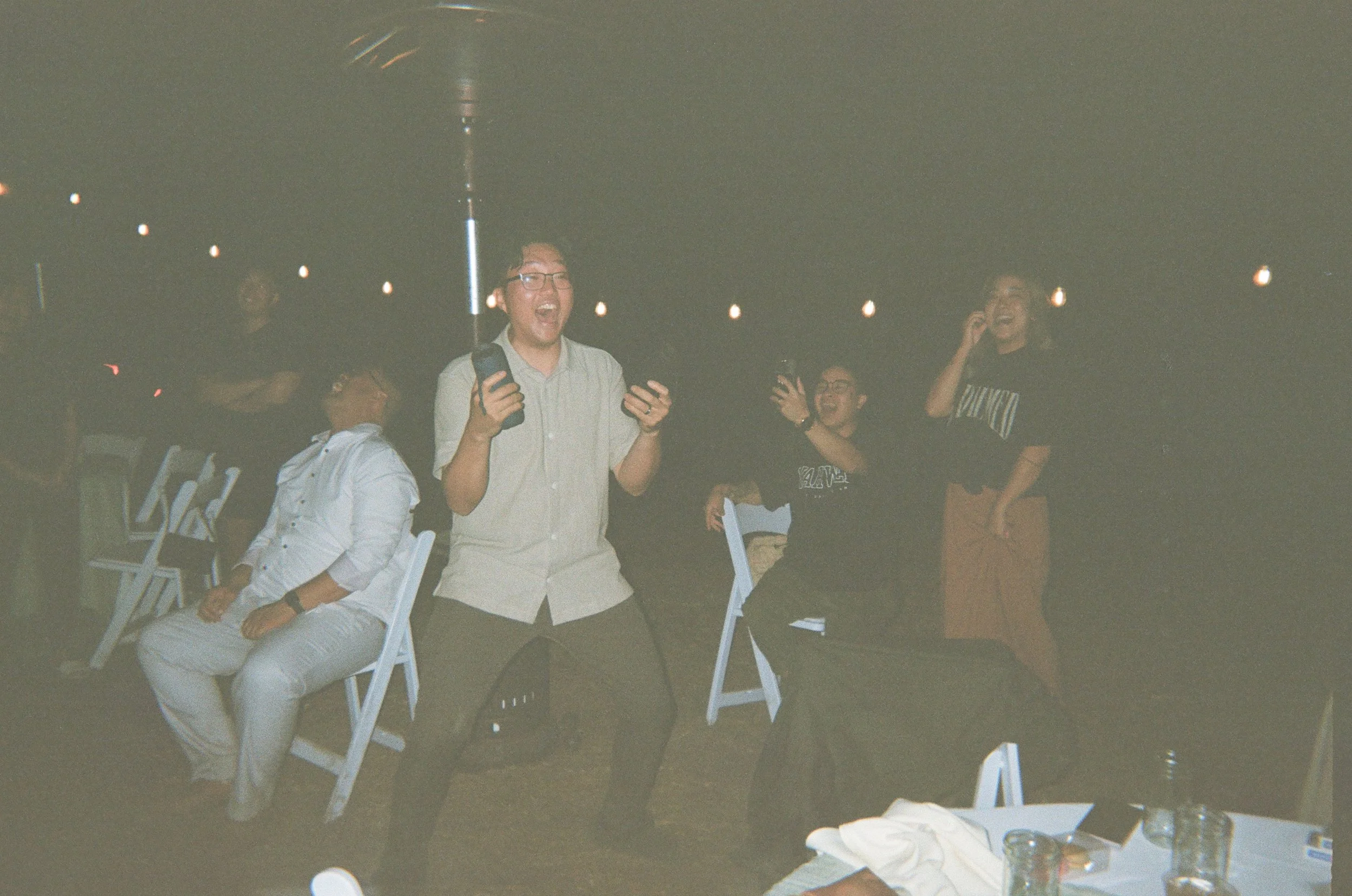 People at a party, some laughing and dancing, in a dark indoor space with string lights overhead.