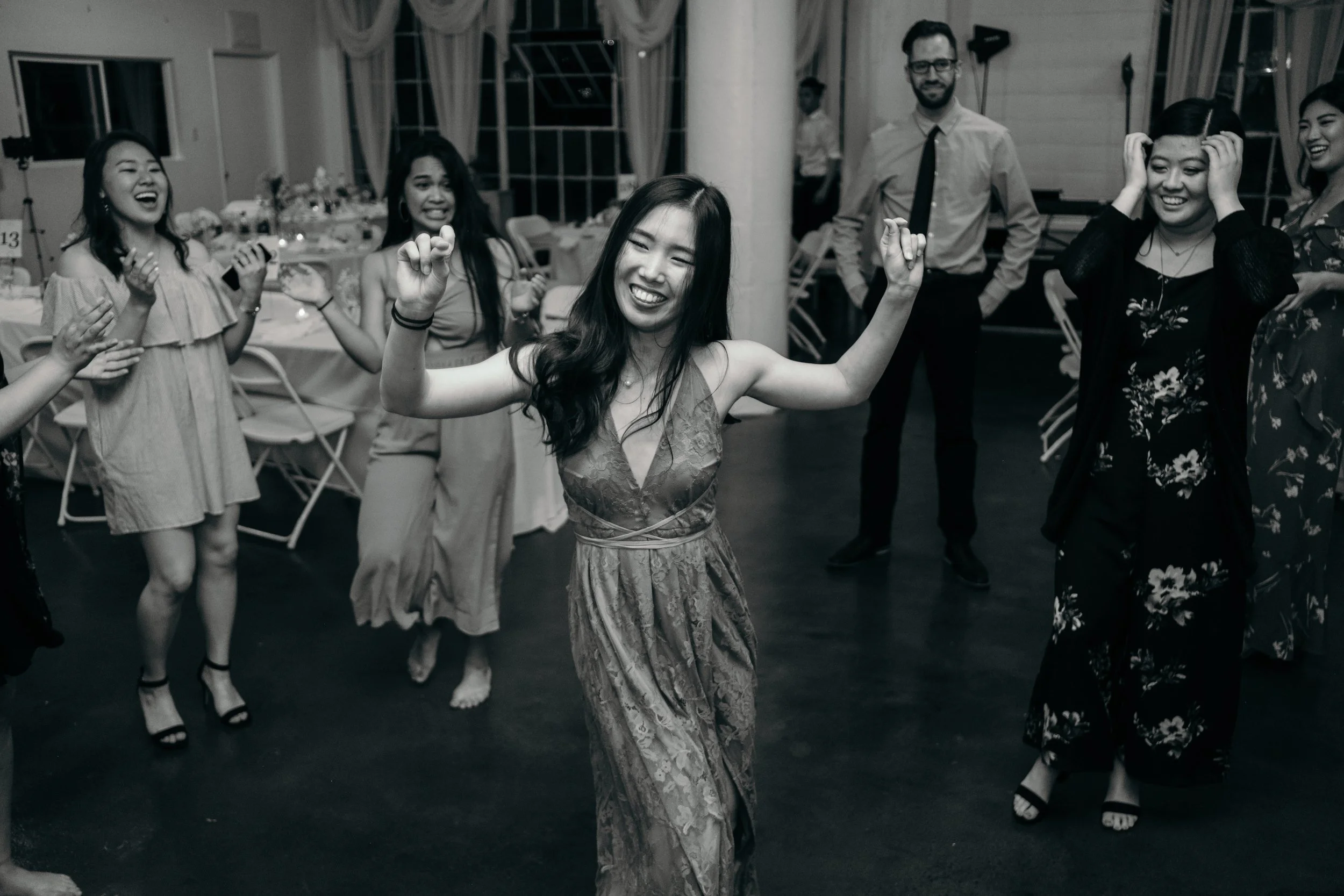 Group of women and a man dancing and celebrating at a social event in a decorated hall.
