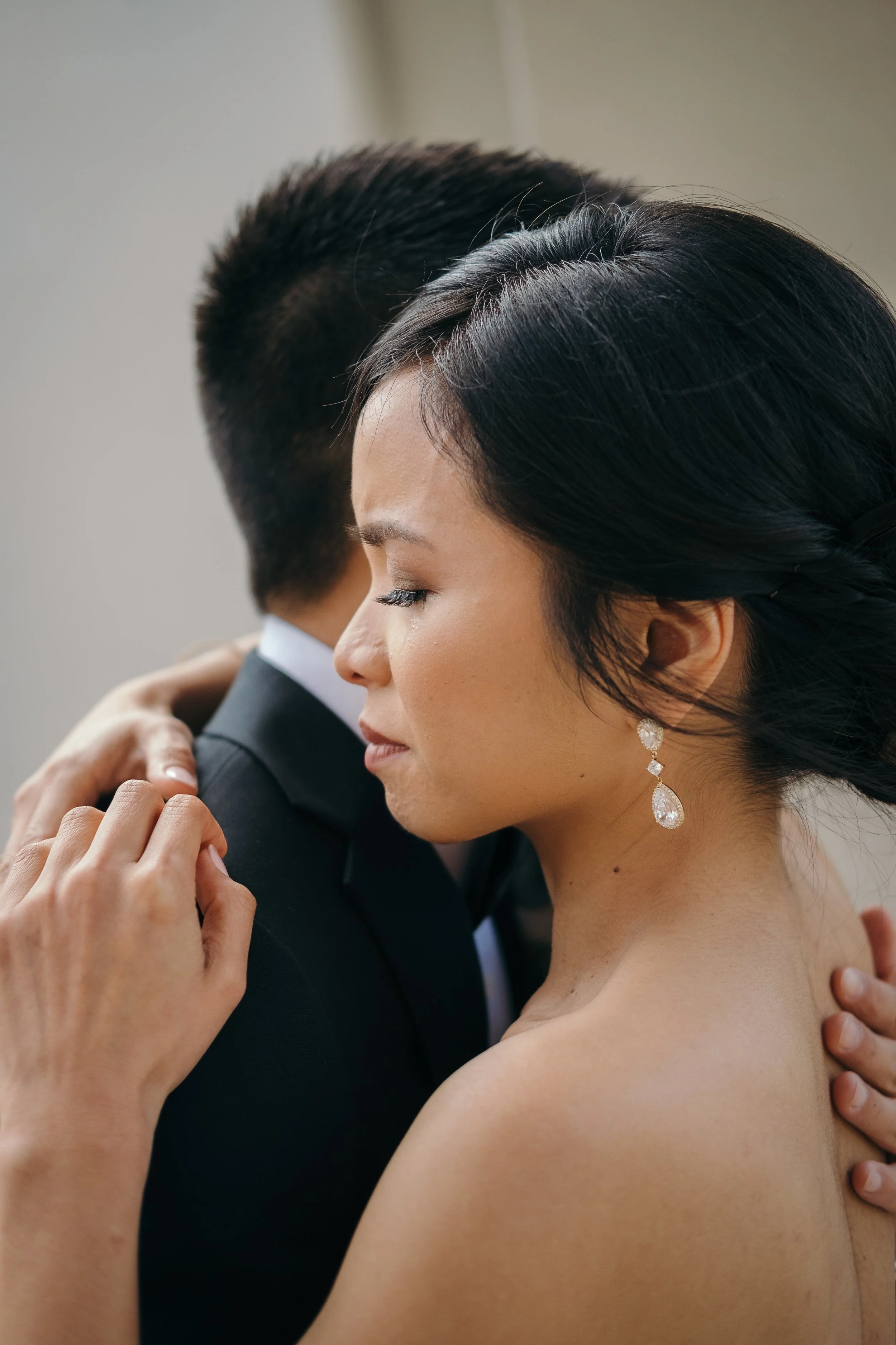 A woman with dark hair and earrings embraces a man in a suit, their eyes closed, in an emotional moment.