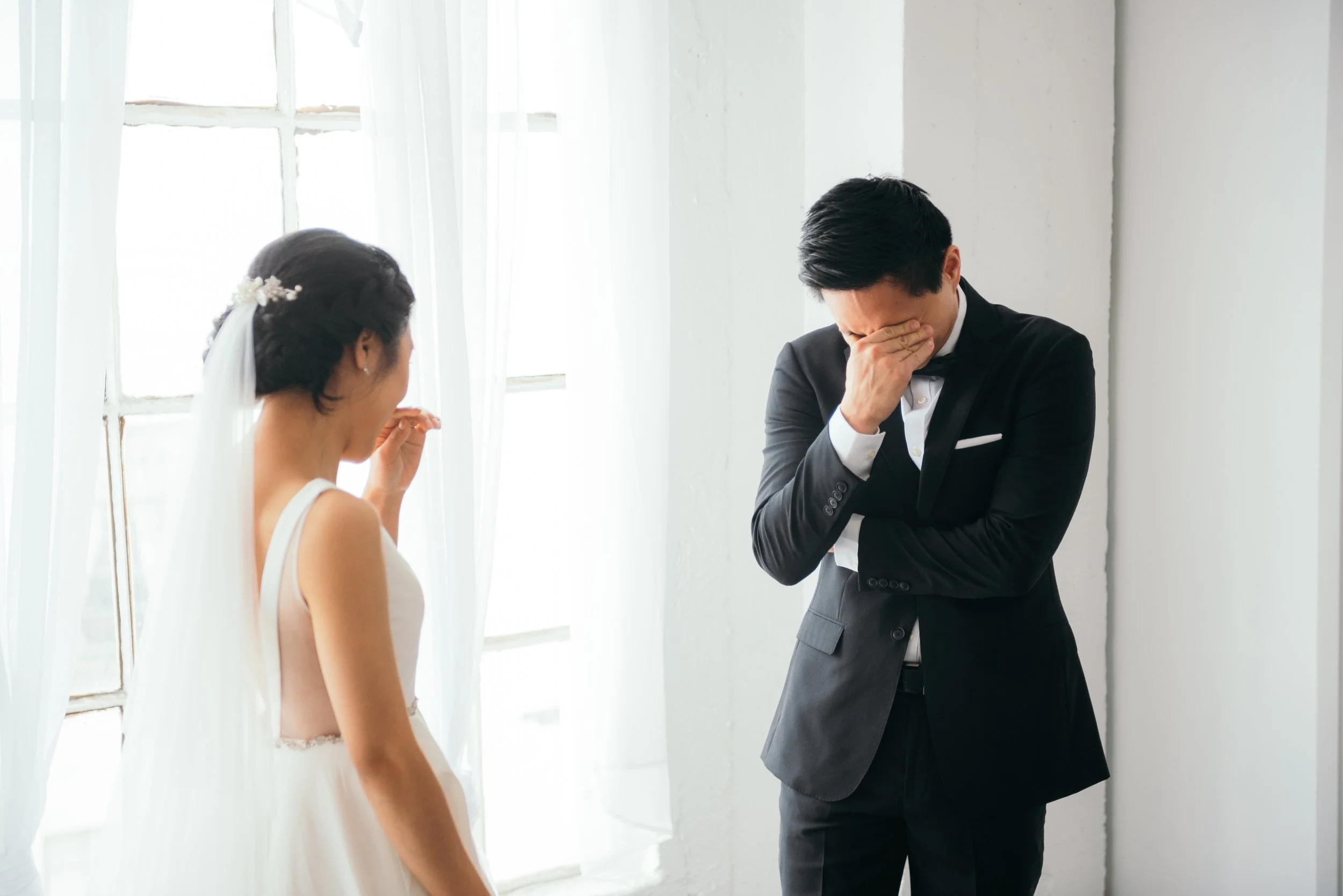 A bride and groom share a heartfelt moment during their wedding, with the groom visibly emotional and wiping his face while the bride looks on with a gentle expression.