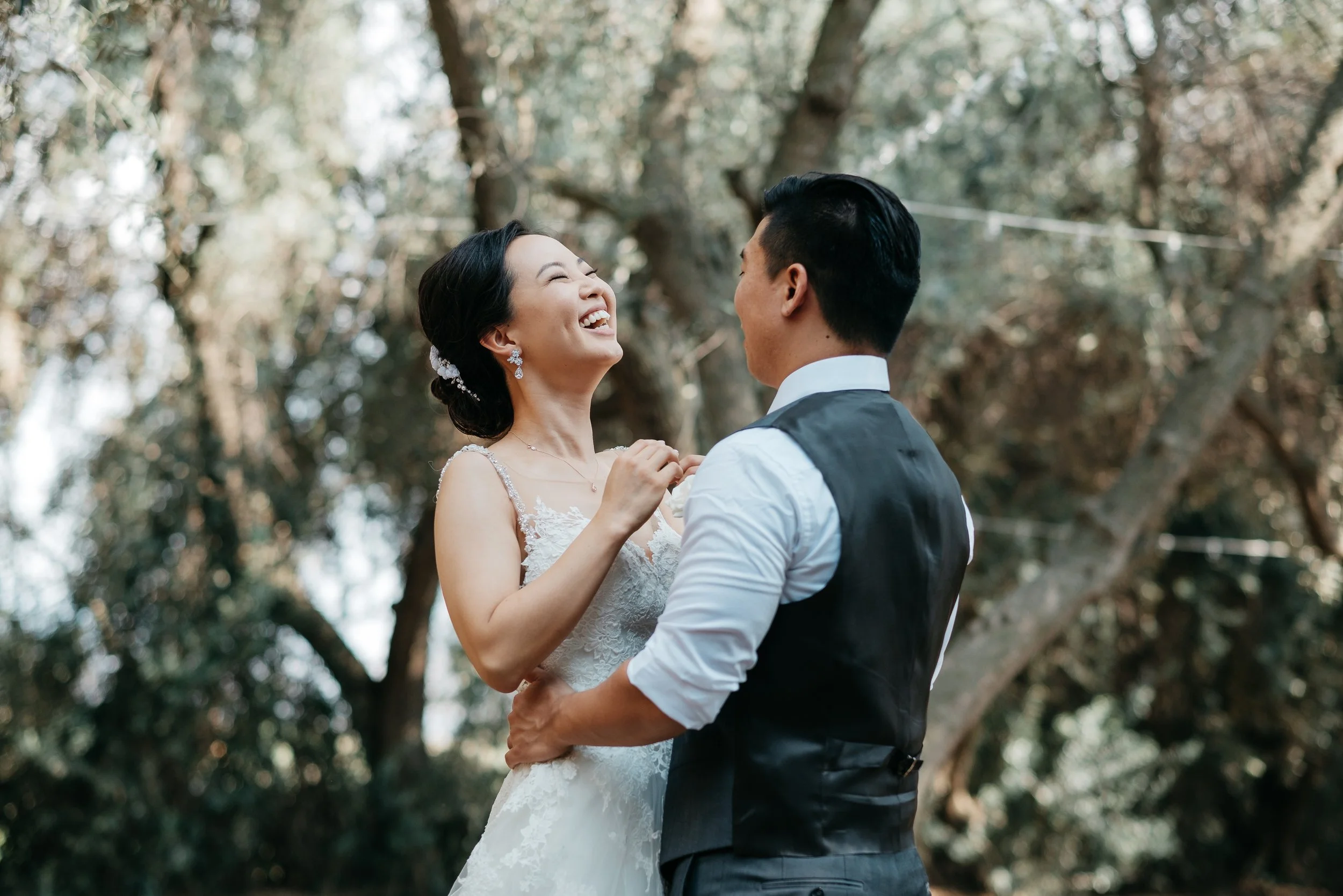 A bride and groom sharing a joyful moment outdoors, with trees in the background.