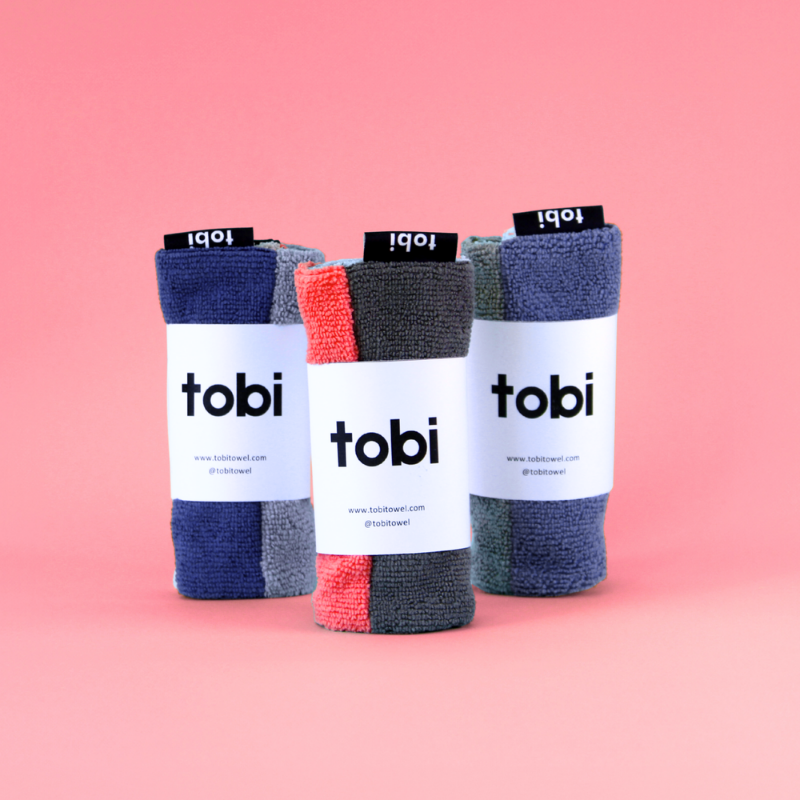 Three rolled-up towels with Tobi branding on a pink background.