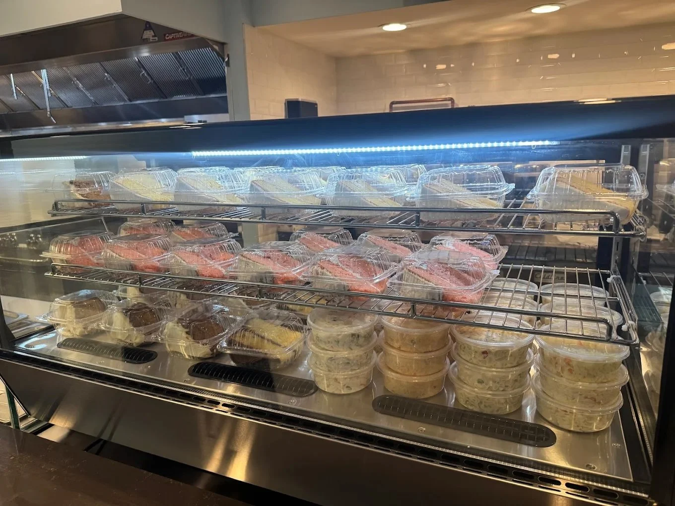A glass display case with multiple shelves containing pre-packaged sandwiches and salads, with a light strip illuminating the items inside.