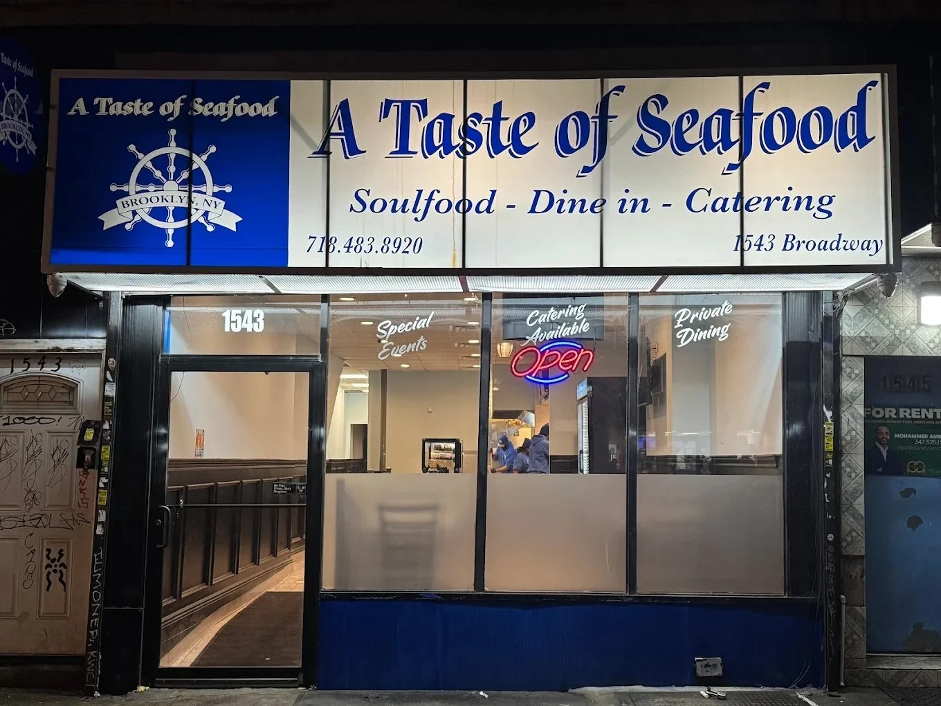 Front view of a seafood restaurant named A Taste of Seafood with signs indicating soulfood, dine-in, catering, and private dining. The restaurant has a neon 'Open' sign in the window, located at 1543 Broadway in Brooklyn, NY. The interior shows staff