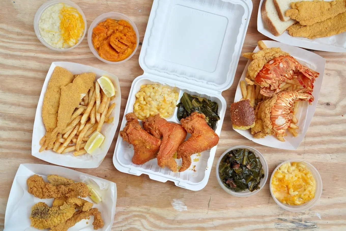 Various Southern comfort foods including fried fish, fried chicken, shrimp, French fries, macaroni and cheese, collard greens, baked sweet potatoes, and breaded fish fillets with lemon wedges.