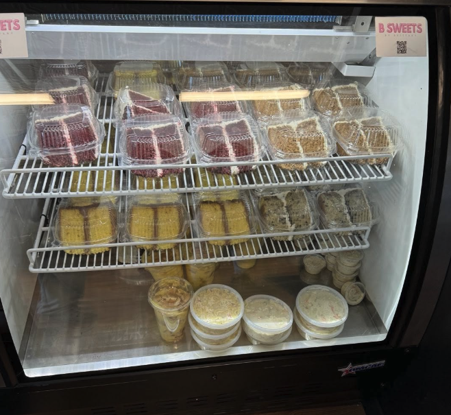 Various cakes and desserts inside a refrigerated display case, including slices and parfaits.