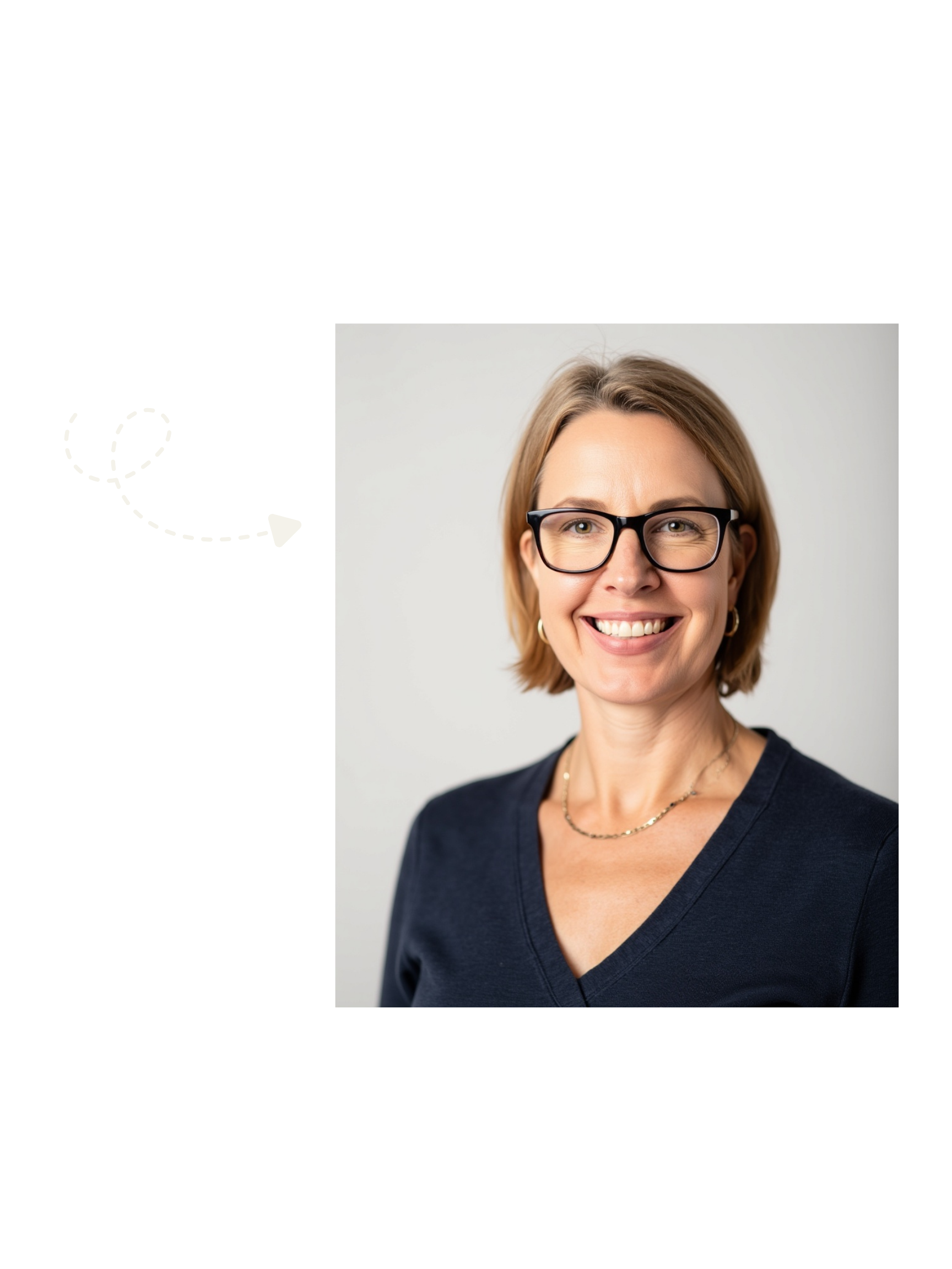 Portrait of a smiling woman with short blonde hair, glasses, wearing a navy blue V-neck shirt, gold jewelry, and hoop earrings, against a plain light background.