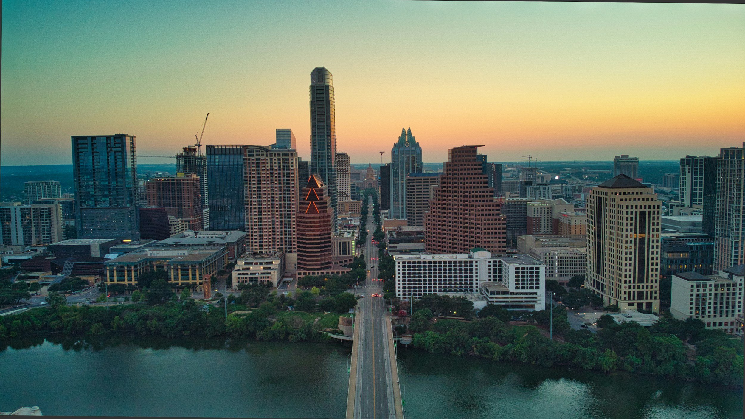 Aerial view of a city skyline during sunset with tall skyscrapers and a river in the foreground.