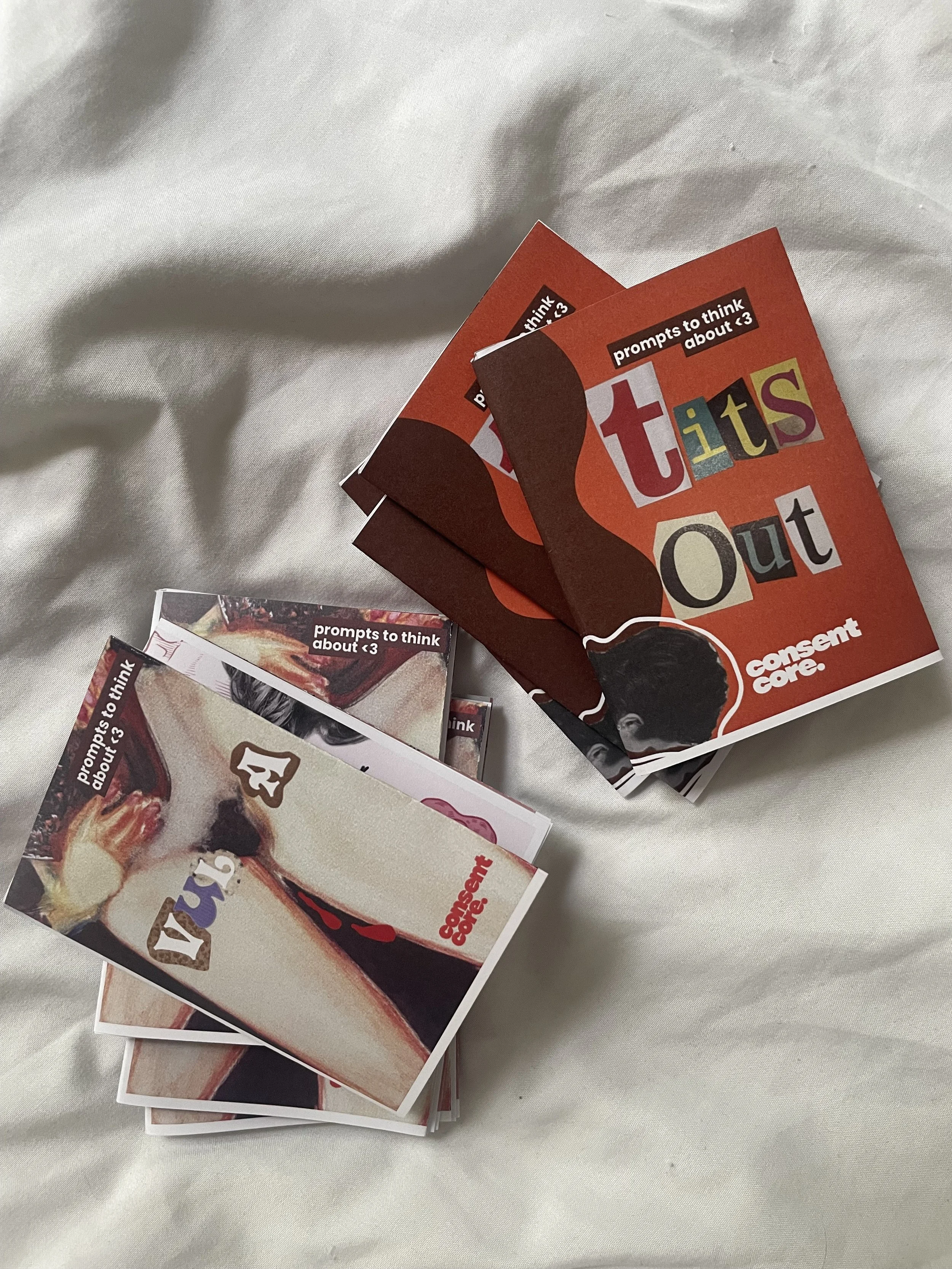 Mehrere Zines mit dem Titel 'prompts to think about <3' liegen auf einem weißen Stoff, die Cover sind bunt gestaltet und zeigen ausdrucksstarke Bilder.