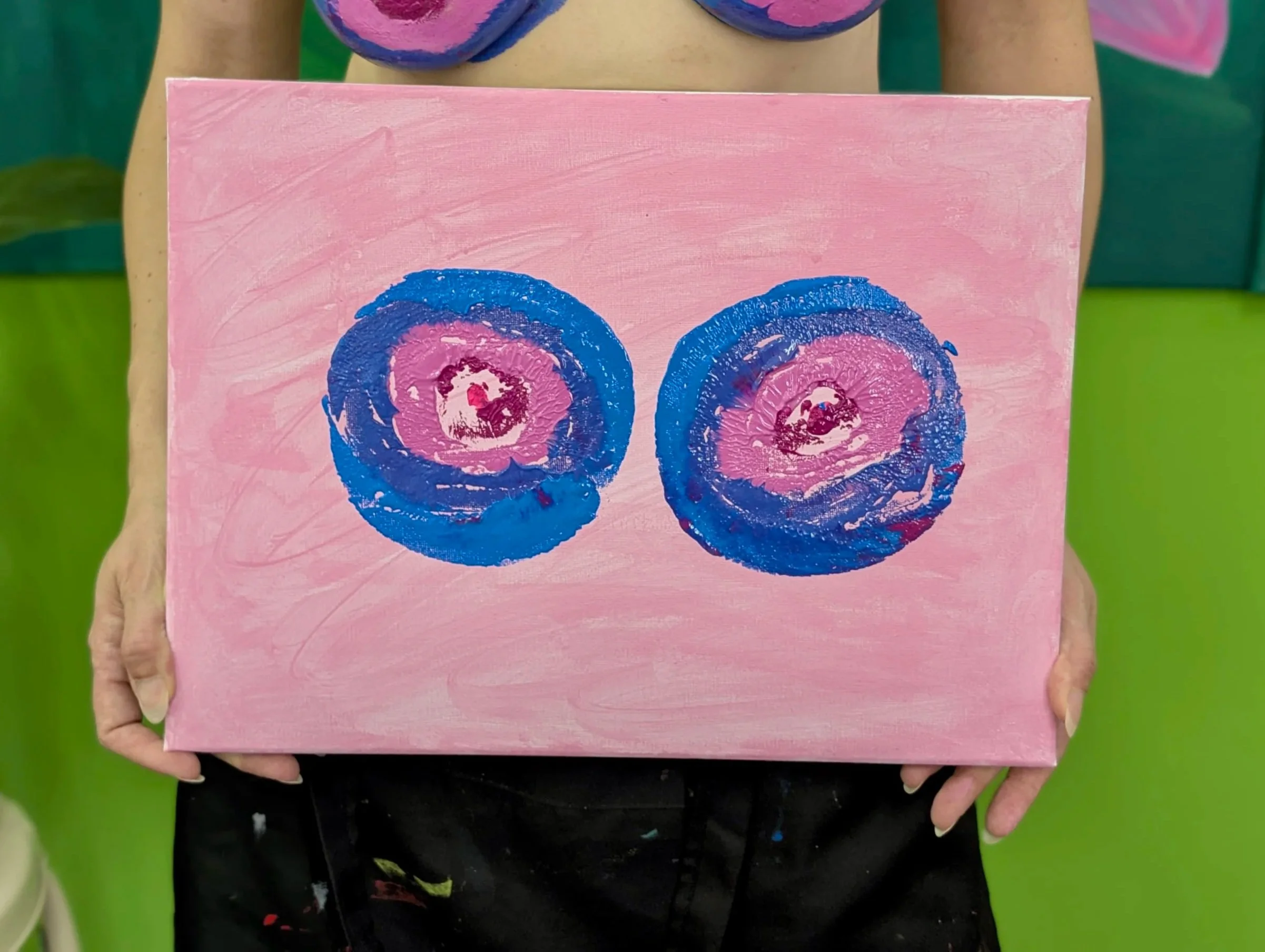 Ein Kunstwerk auf einer pinken Leinwand mit zwei blauen, rosafarbenen und weißen spiralförmigen Mustern, gehalten von einer Person vor einem grünen Hintergrund.