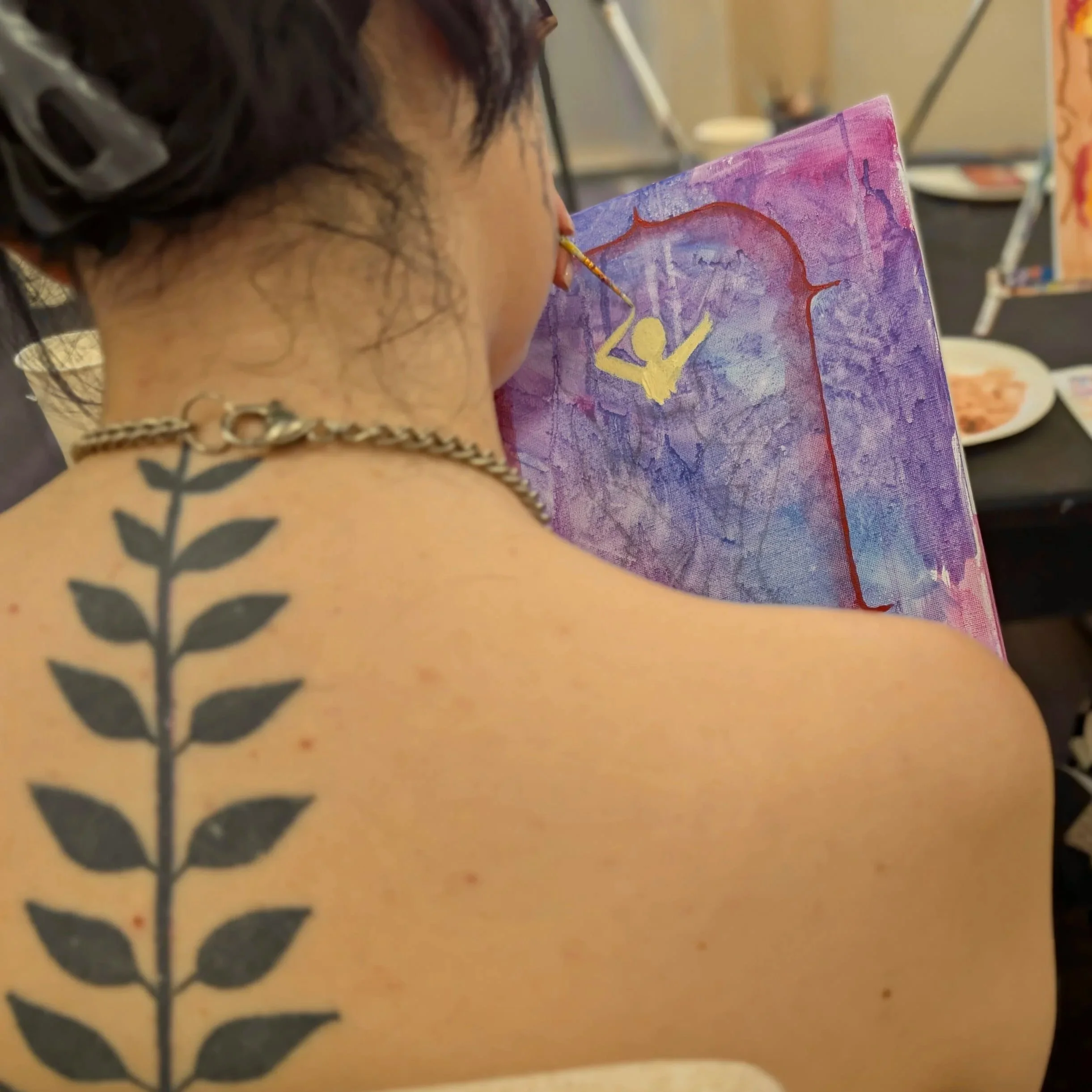 Eine Person malt mit einem Pinsel auf eine Leinwand, die bunte Farben und eine gelbe Figur zeigt.