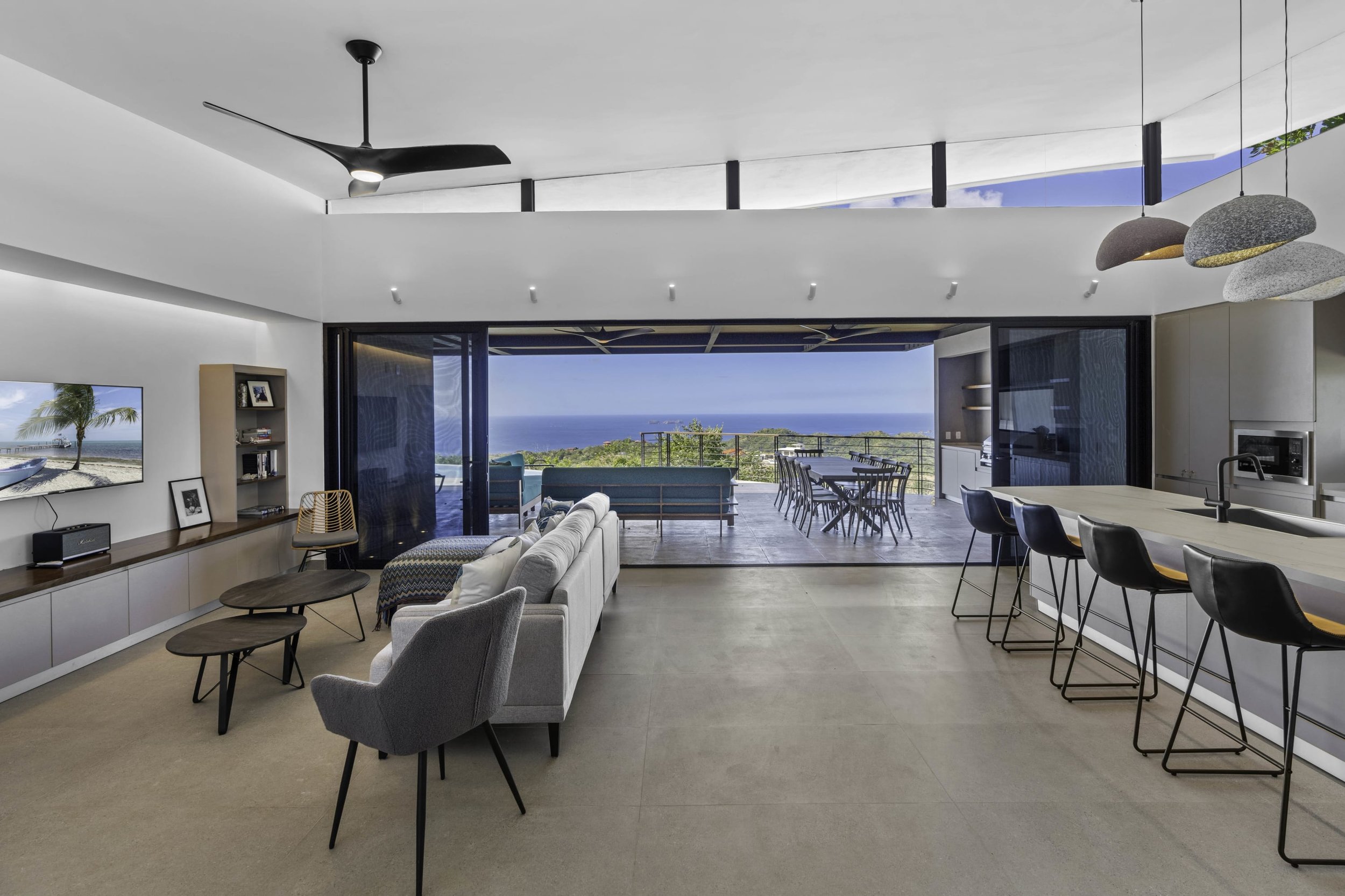 Modern open-concept living space with a view of the ocean, featuring a living area, dining area, and kitchen, with large sliding glass doors opening to a balcony.