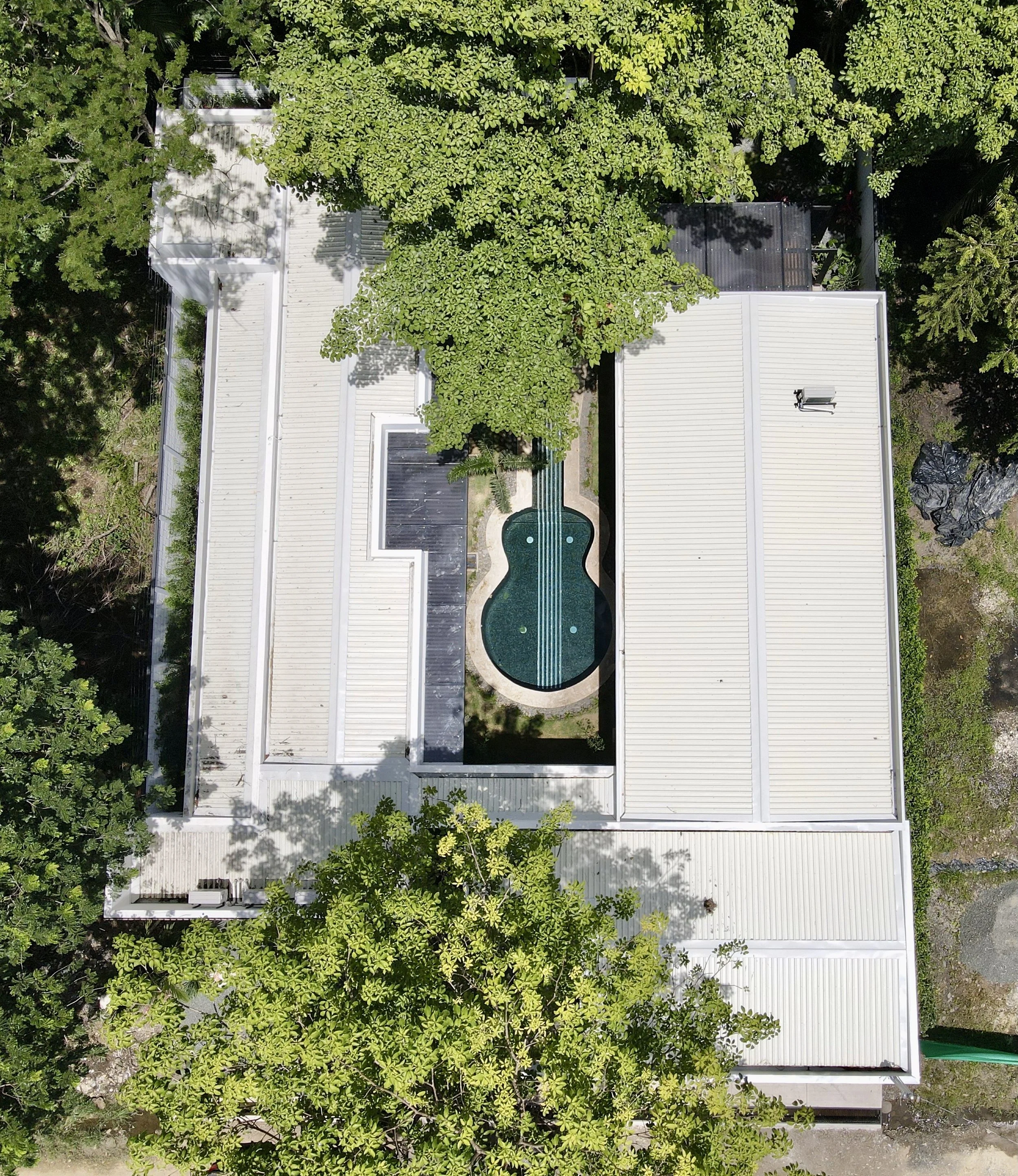 Top-down view of a house with a white roof, surrounded by green trees and a small yard with a spiral-shaped pool.