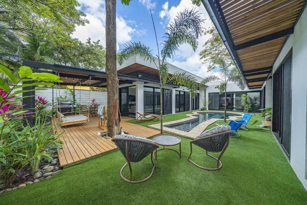 Modern backyard with a swimming pool, lounge chairs, wooden deck, green lawn, and tropical plants.