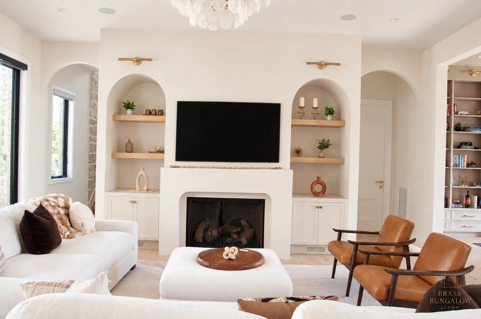 Prentice living room with a curved plaster fireplace, oak shelves, cream sofas and cognac leather chairs.