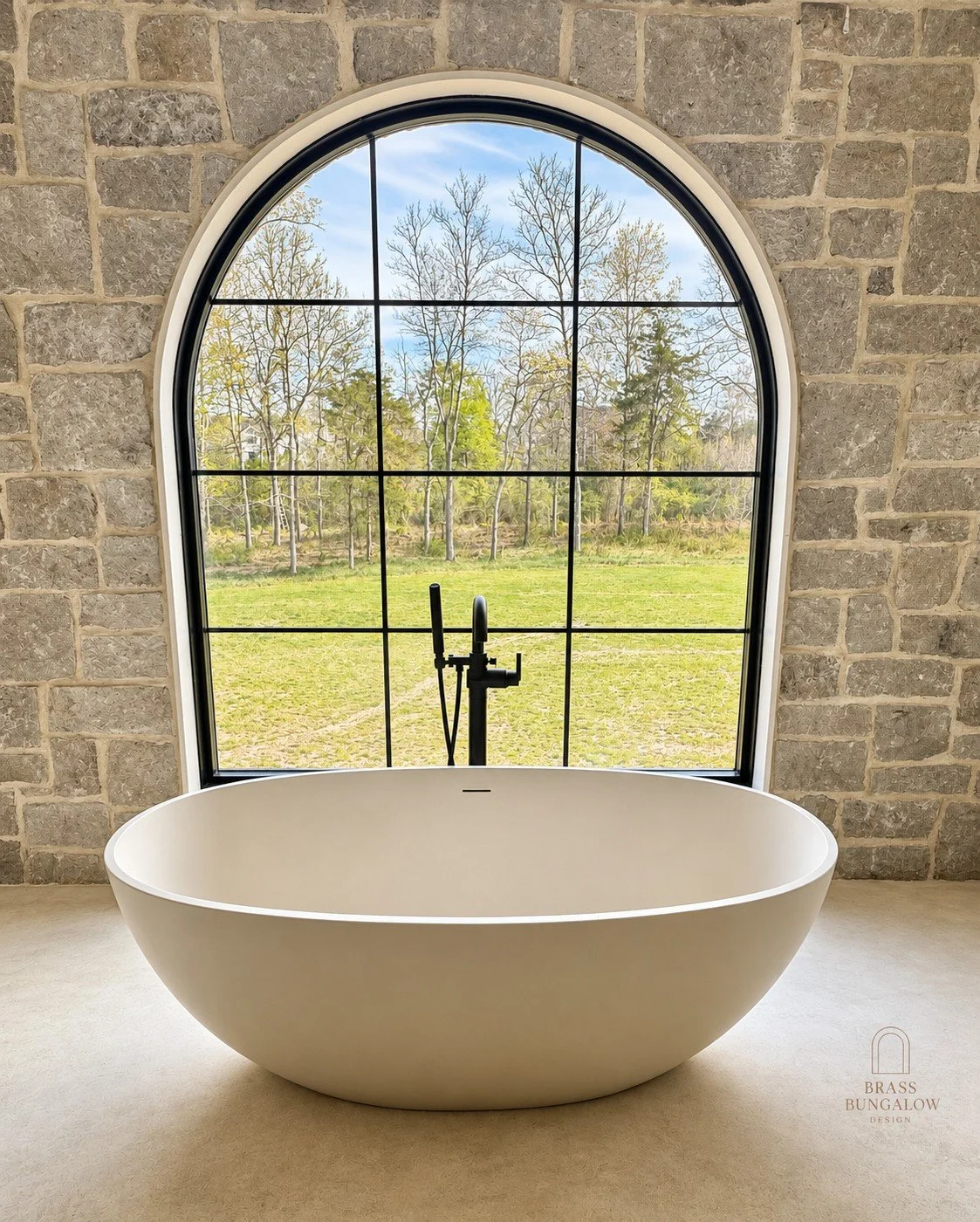 Freestanding bathtub framed by an arched black steel window and natural stone walls at Prentice.