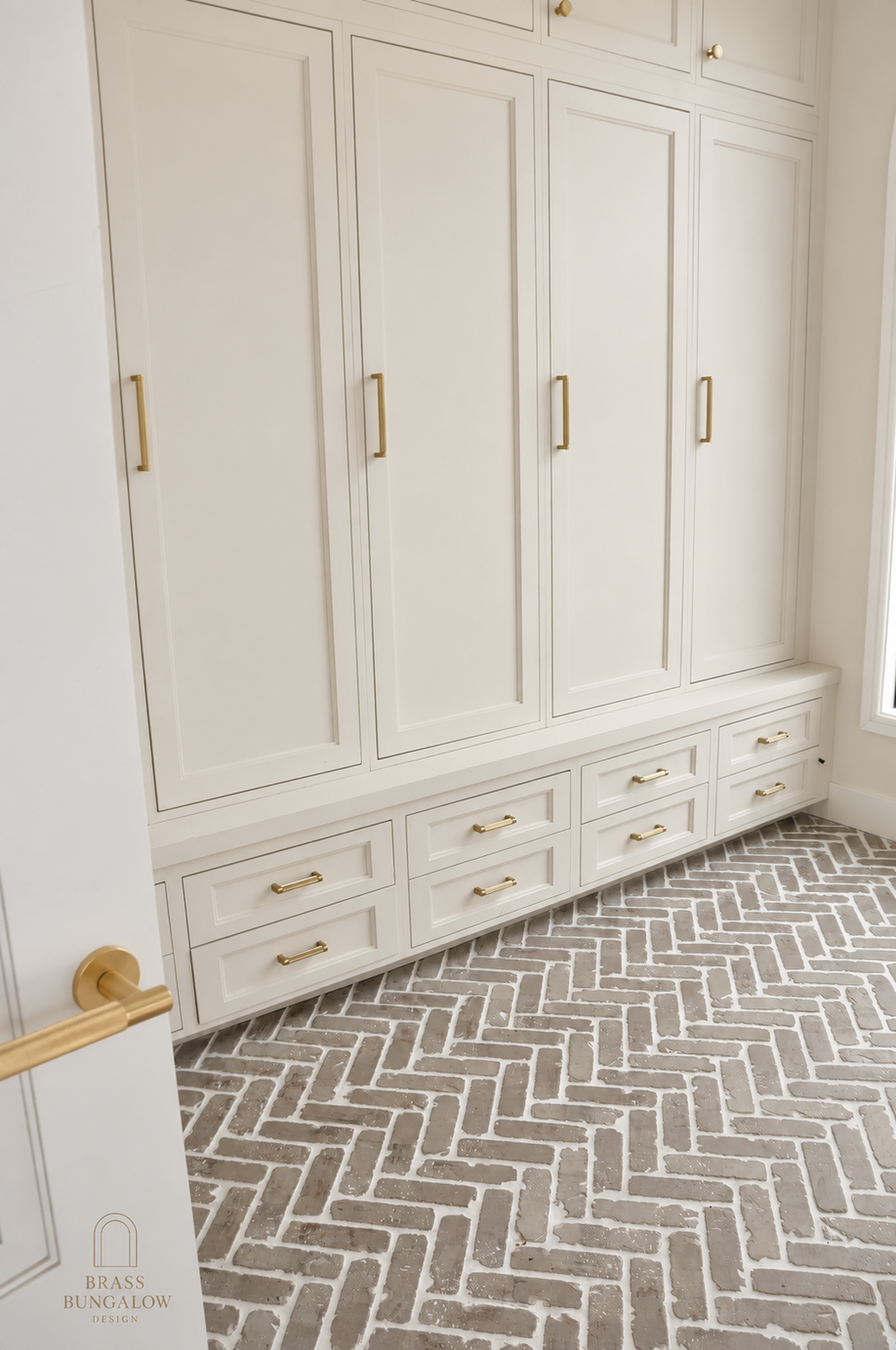 Warm beige mudroom cabinetry and herringbone brick flooring