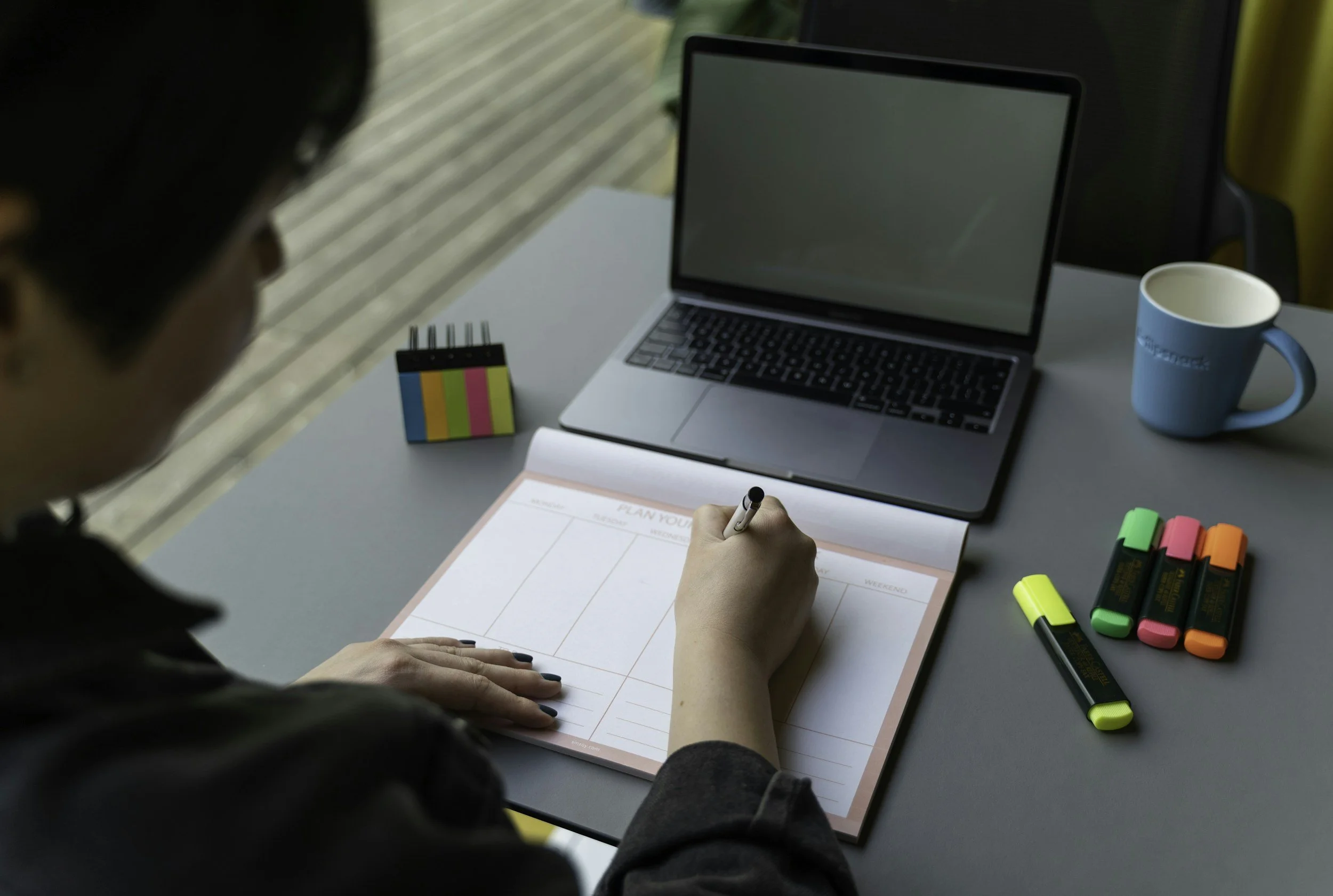 Student taking notes beside a laptop while studying