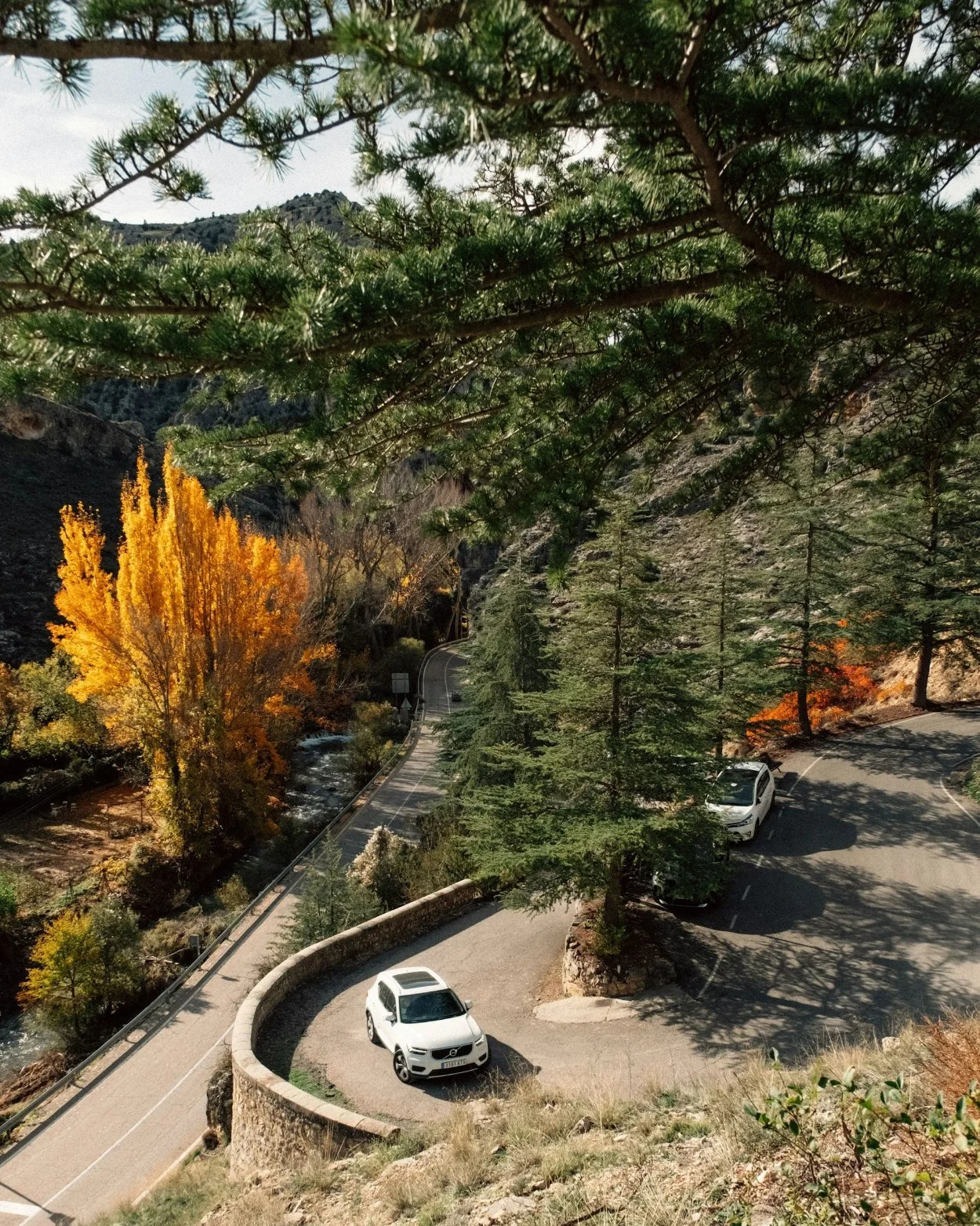 White car on a hairpin bend of a mountain road in Albarracín, Spain, with autumn trees